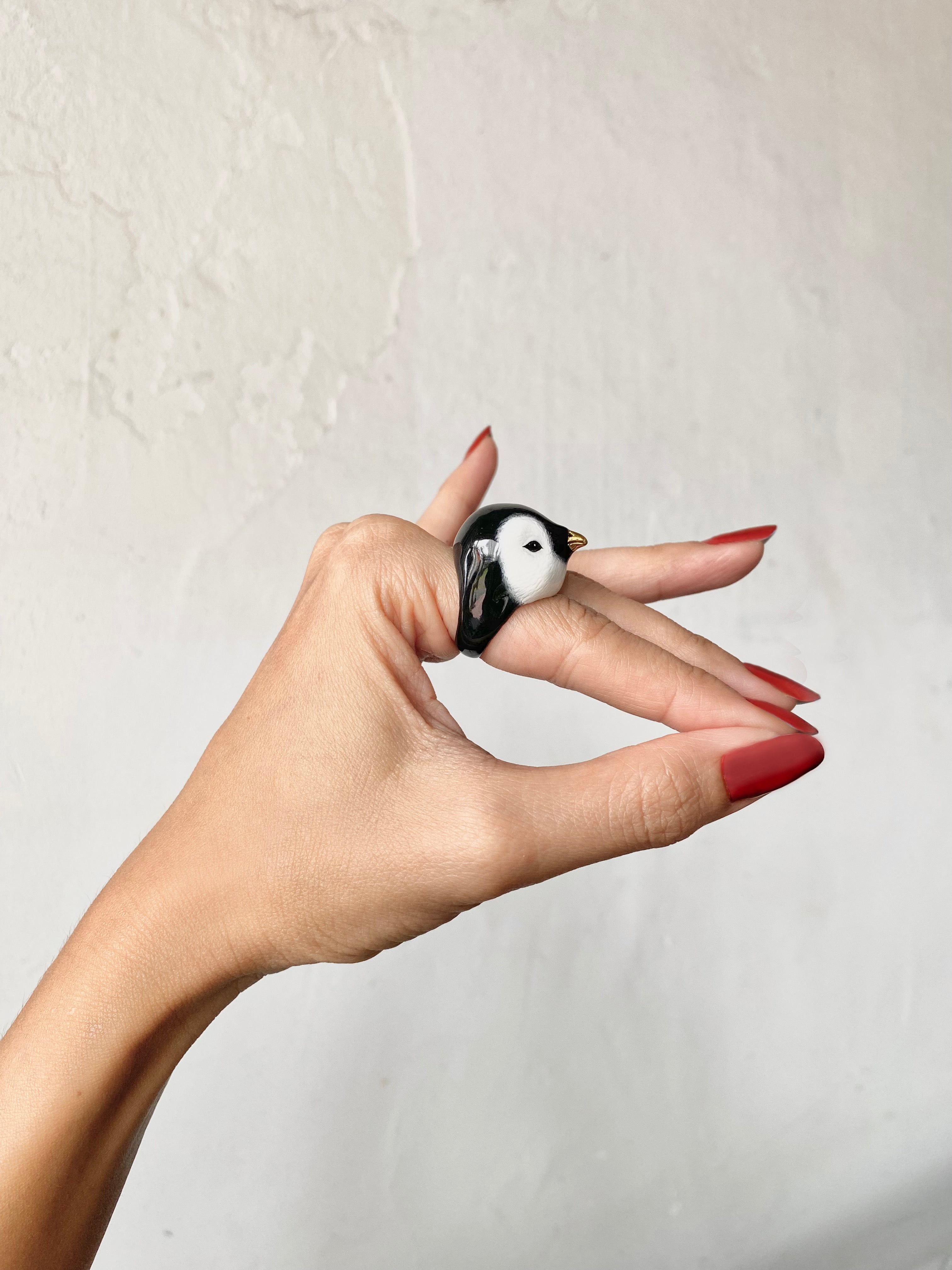 lose-up of a cute penguin ring showcased on a hand with red nails.