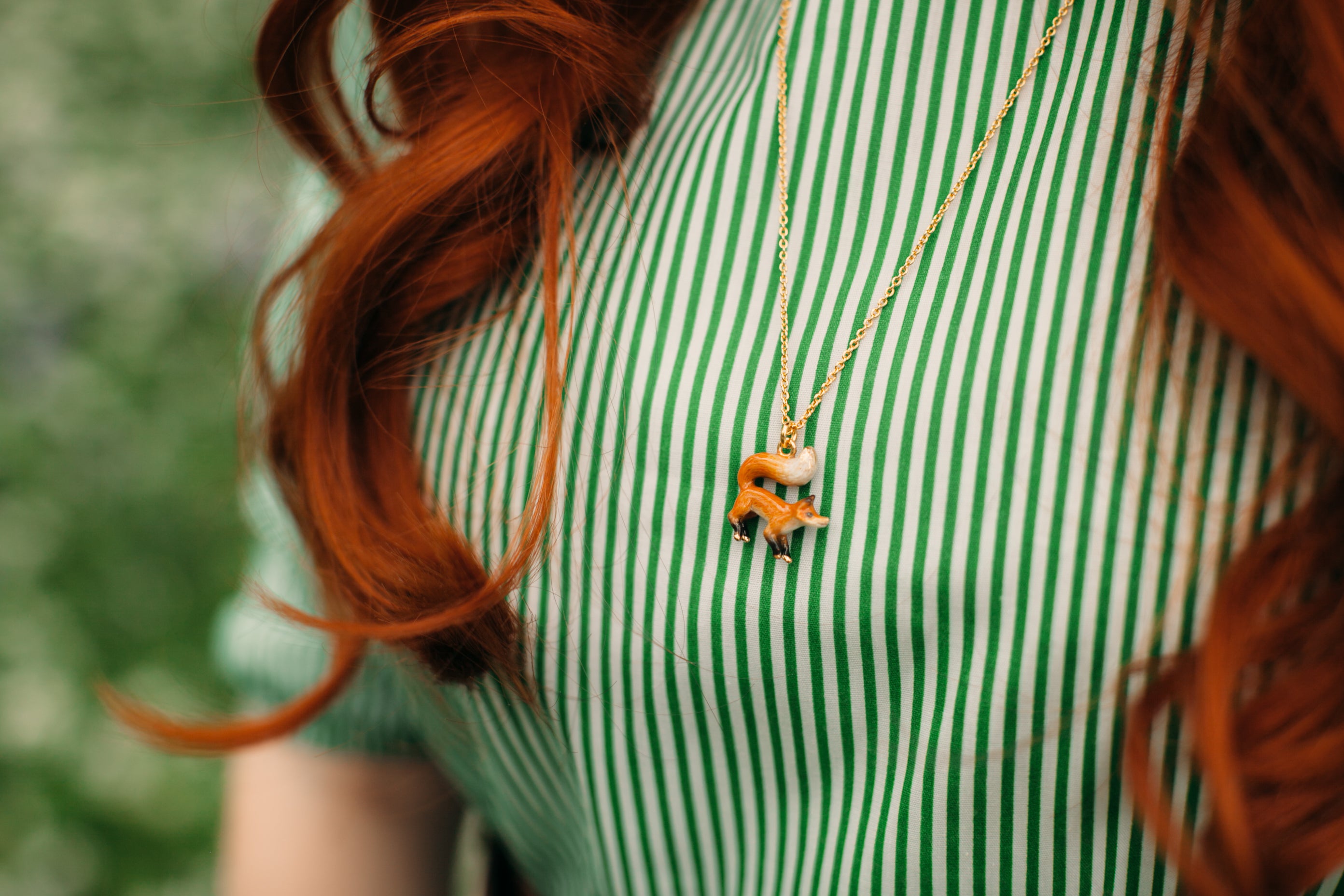 Handcrafted and hand-painted fox necklace worn on a green striped shirt.