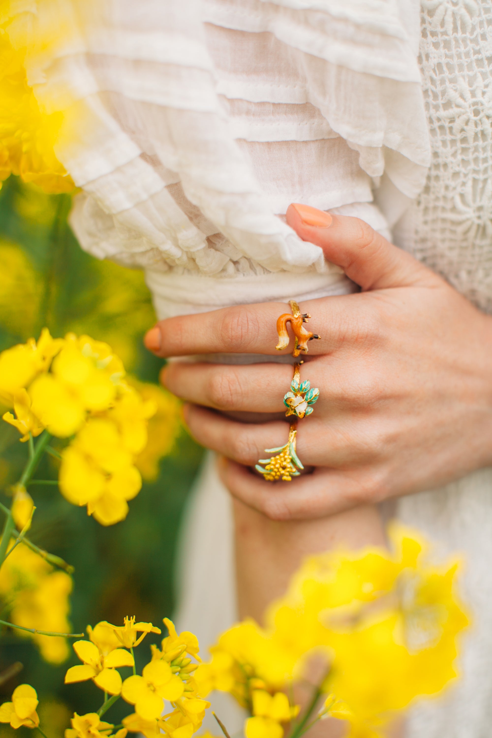 Trio ring set featuring a fox, floral, and butterfly designs on a hand among yellow flowers.