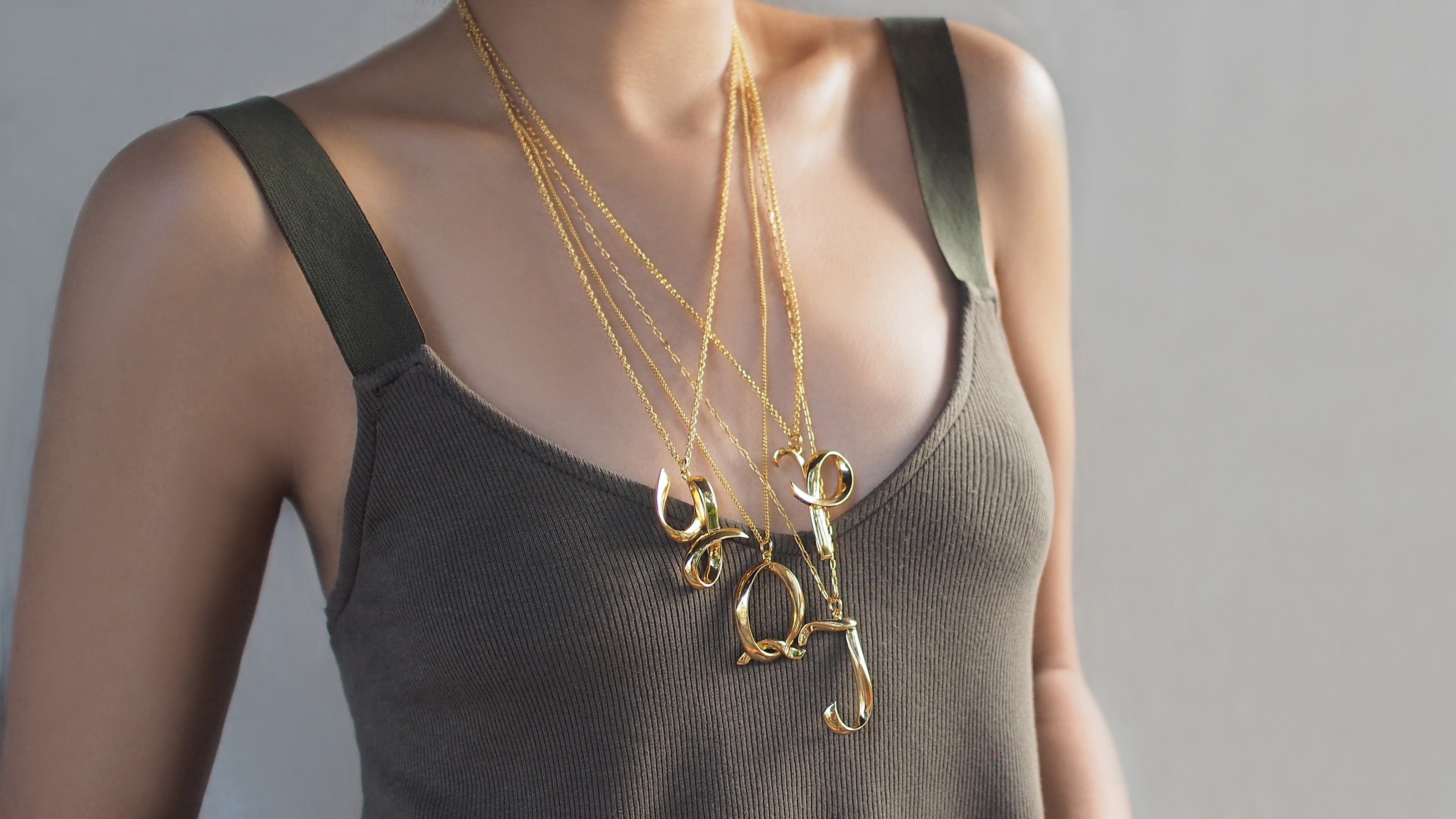 Close-up of layered, elegant, gold-colored letter necklaces on a casual outfit.