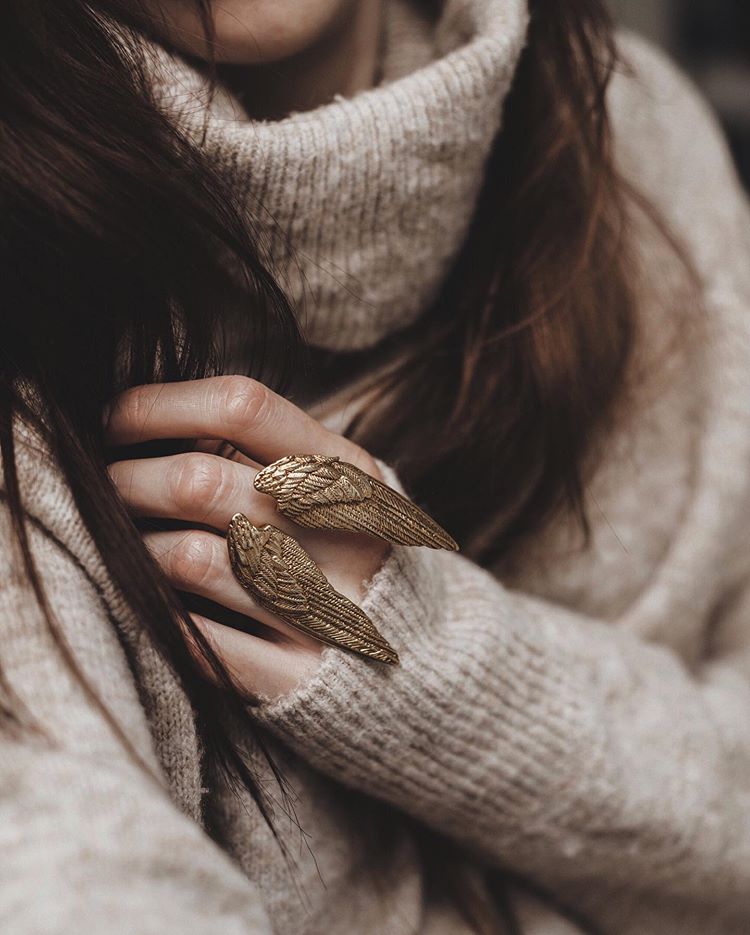 A beautiful golden wing ring worn on a hand, paired with a cozy sweater.
