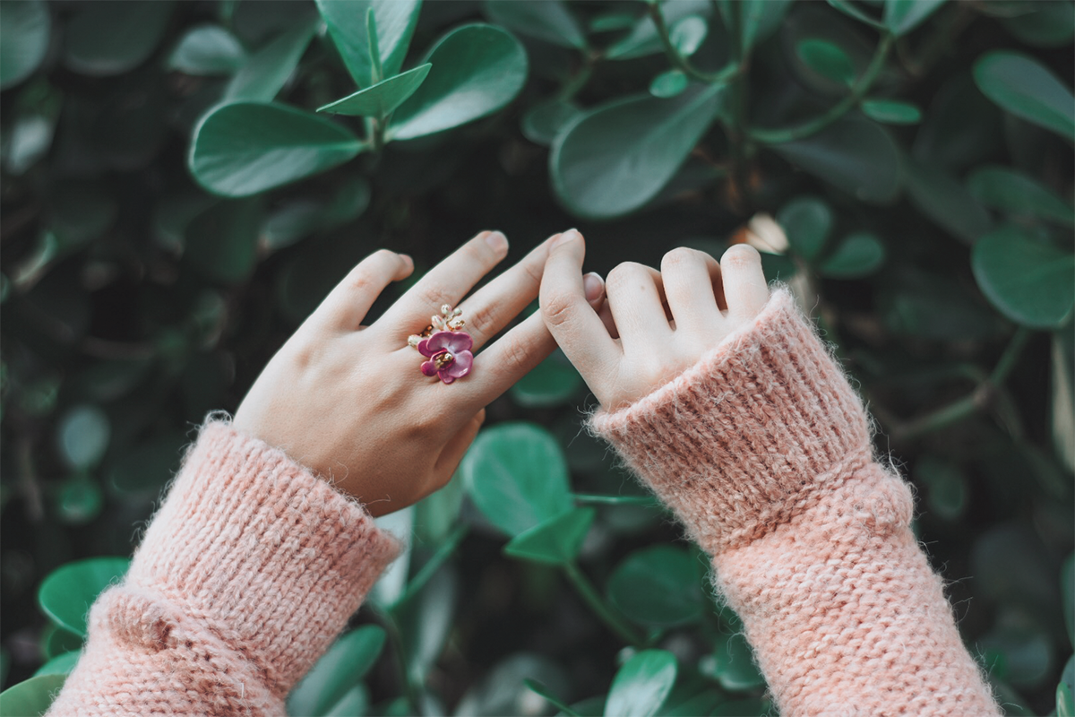 Close up of a hand wearing a floral ring feating a purple phalaen design in natural scene.