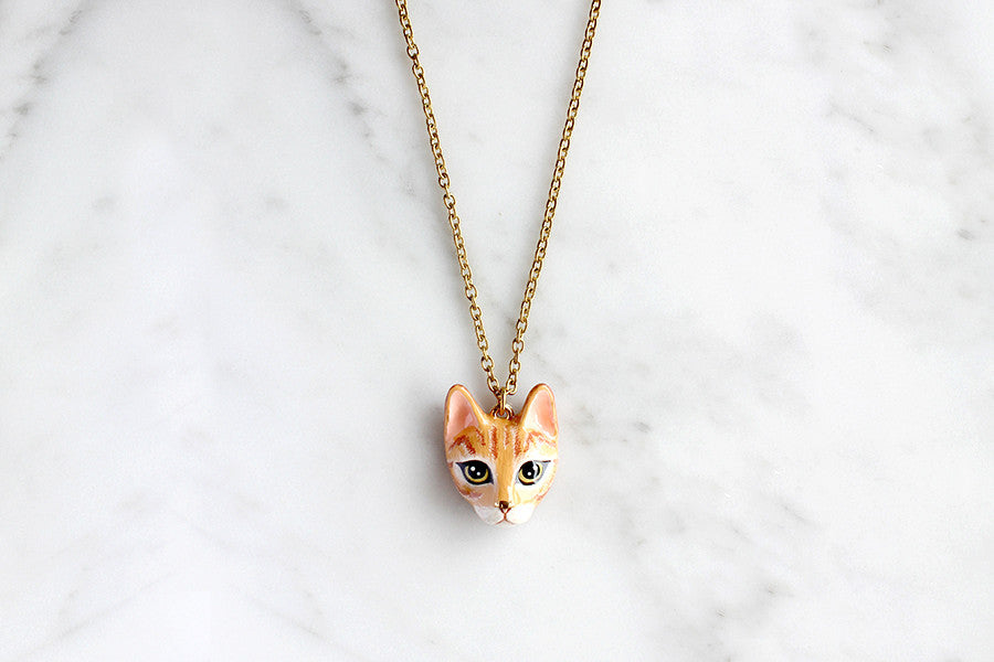 Adorable orange cat pendant necklace placed on marble background.