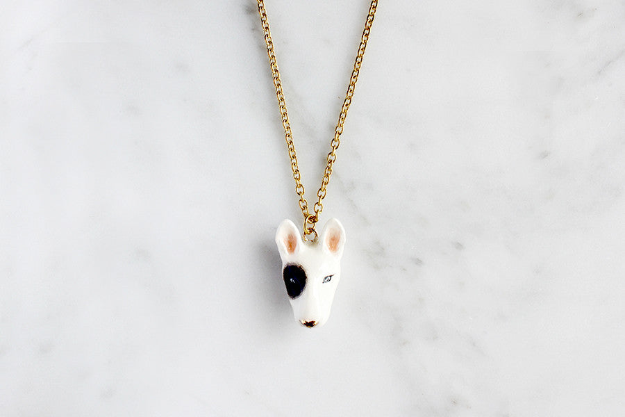 Unique Bull Terrier dog head pendant necklace with gold chain on marble background.