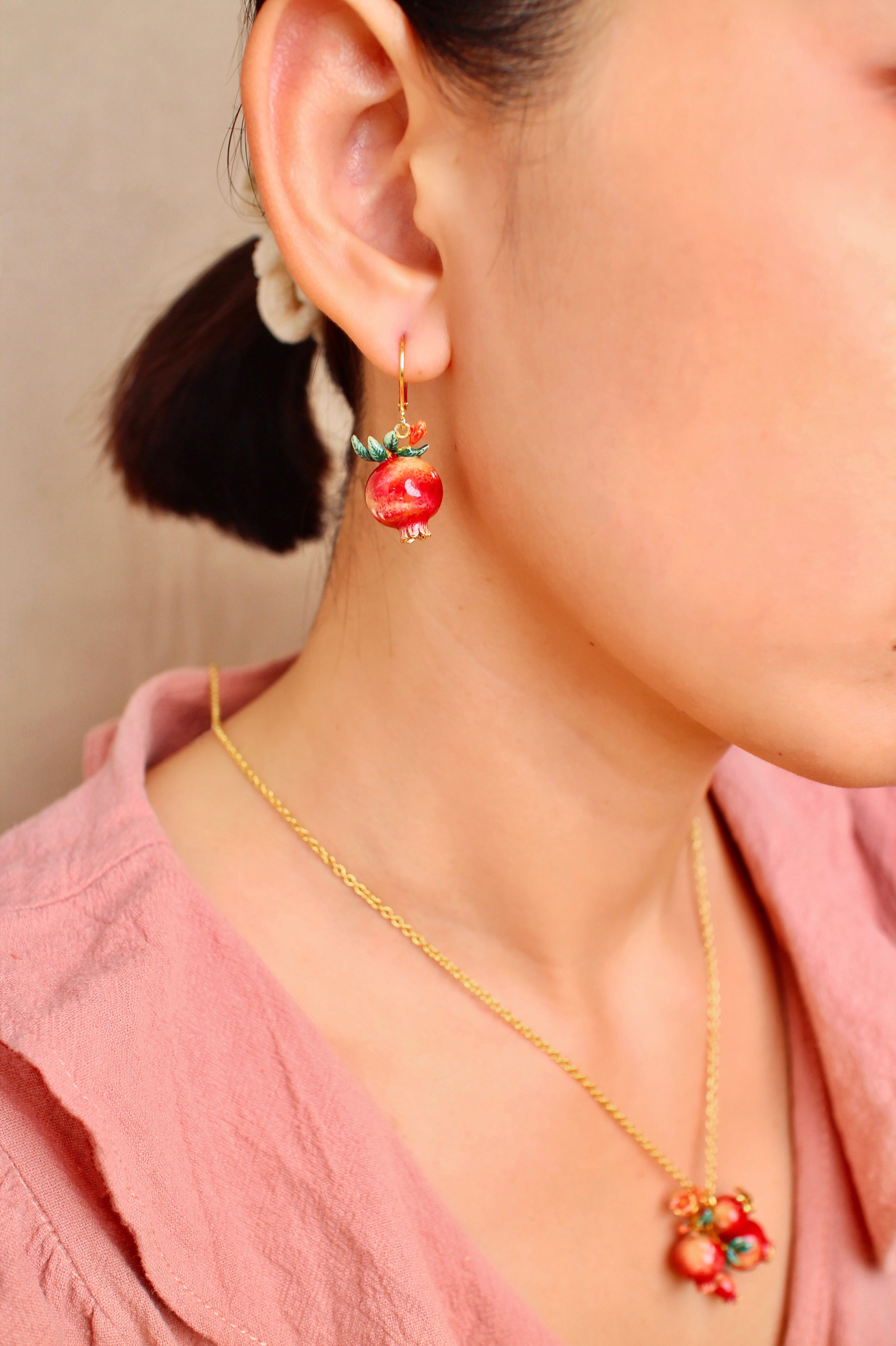 A close-up of a woman wearing charming pomegranate earrings and a matching necklace