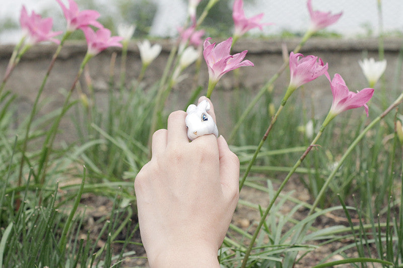 An adorable rabbit ring worn on a hand amidst blooming flowers in a garden.