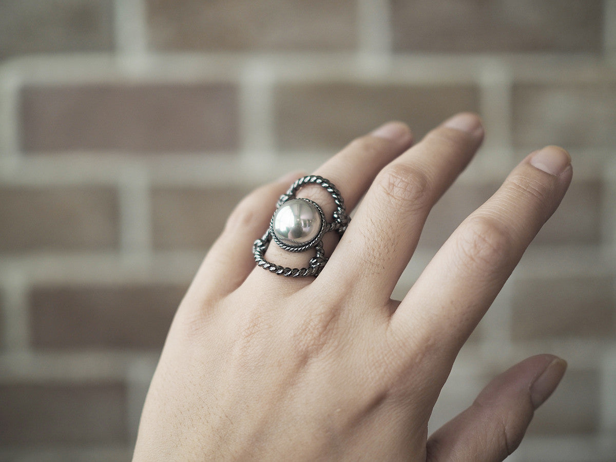 Close-up of a hand wearing a unique ring with a large costume pearl surrounded by twisted rope design.