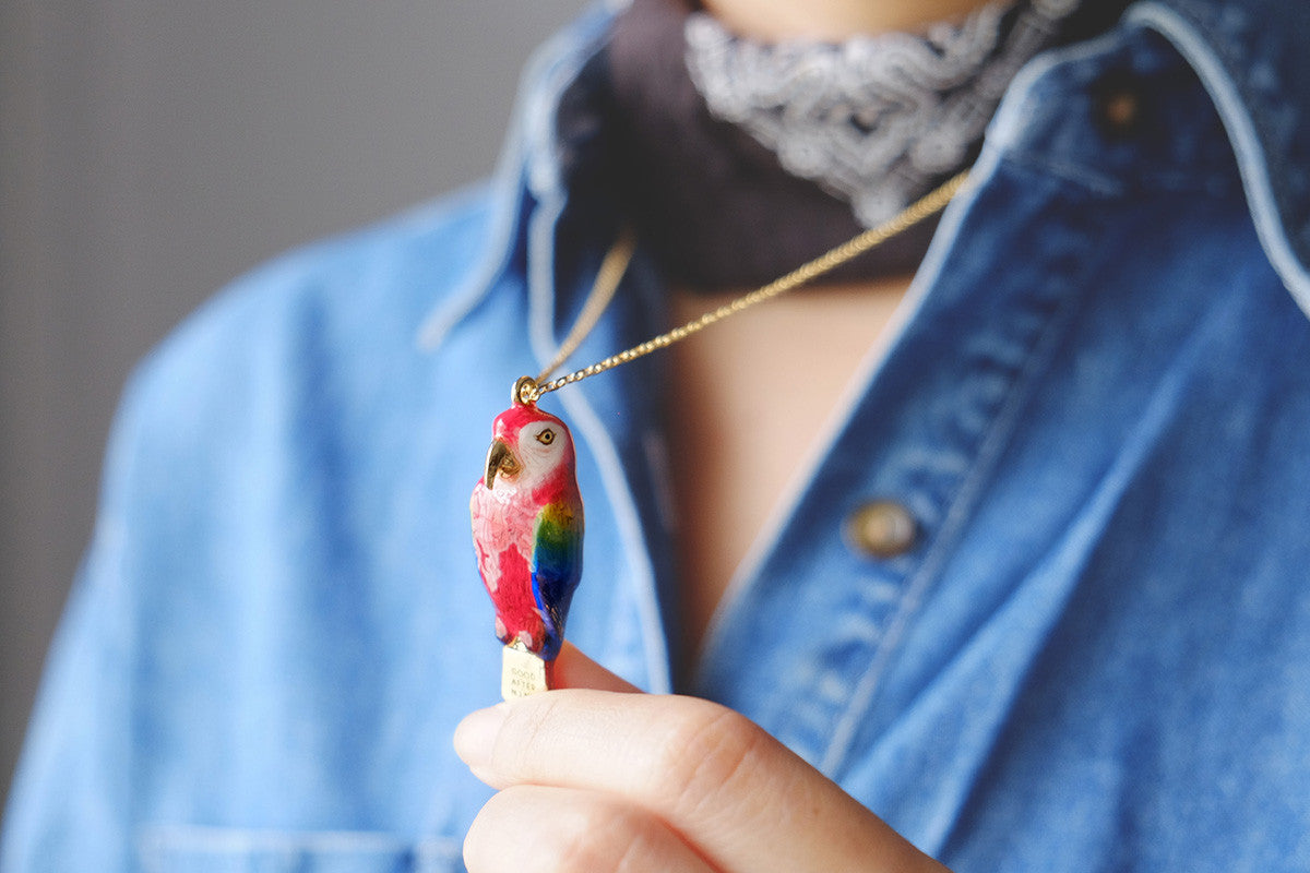 Colorful parrot-shaped whistle necklace being held by a person wearing a denim shirt.