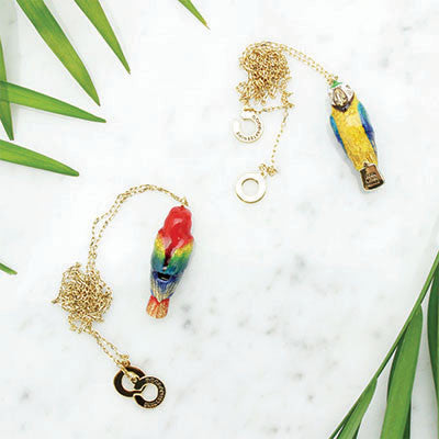 A collection of colorful bird whistle necklaces featuring a parrot, and macaw on a marble background.