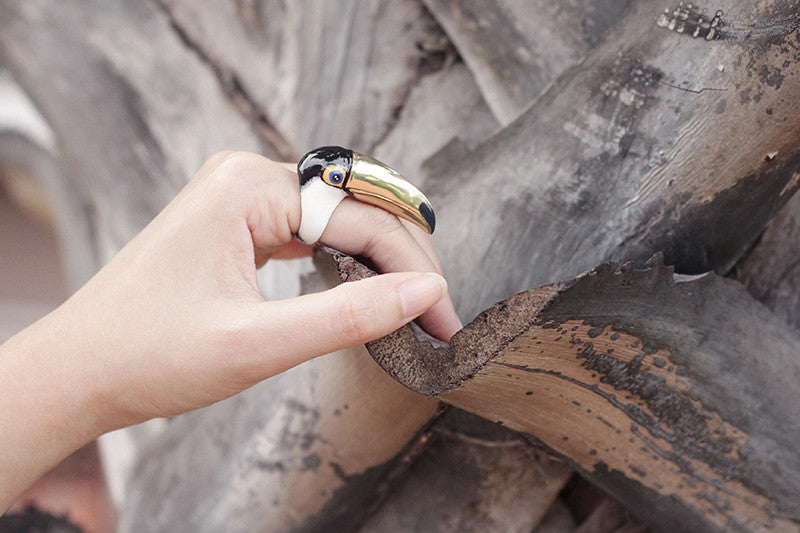 Hand wearing a toucan-shaped ring, gently grasping a textured piece of bark.