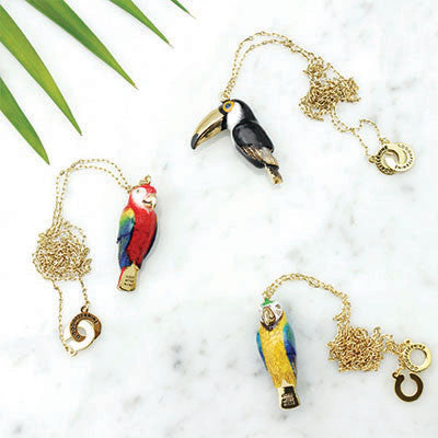 A collection of colorful bird whistle necklaces featuring a parrot, macaw, and toucan on a marble background.