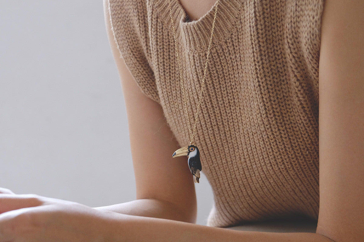Close-up of a person wearing a toucan whistle necklace with a gold chain and casual outfit.