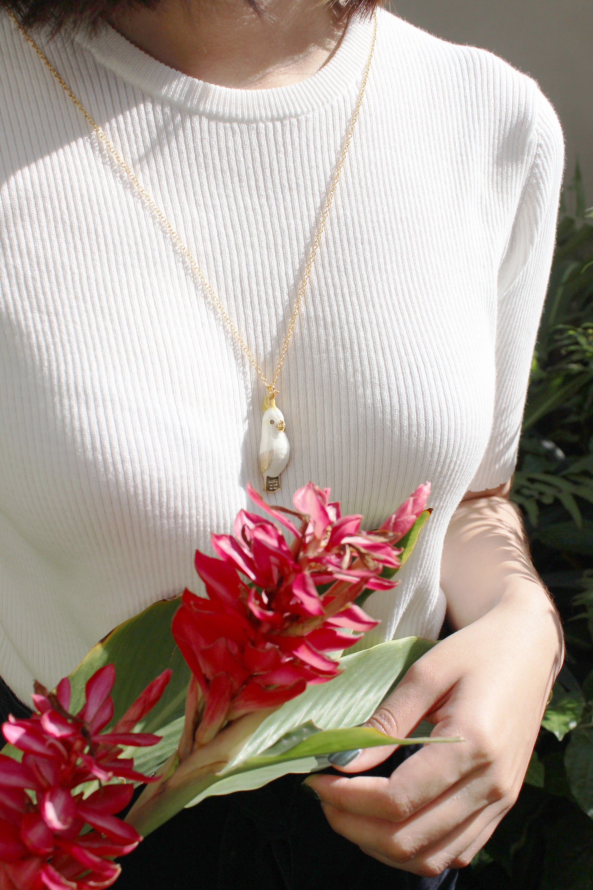 A close-up of an adorable cockatoo whistle necklace worn on a person with causal outfit, surrounded by natural setting.