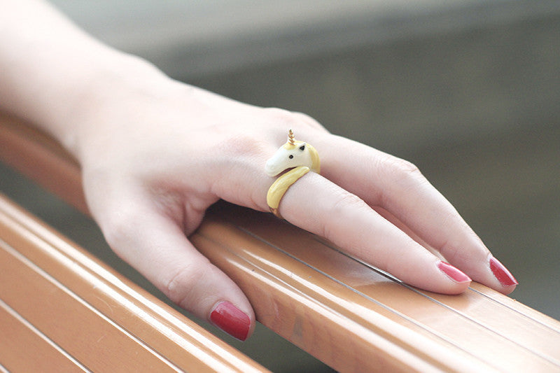 A close-up of a hand wearing a unicorn ring with red nails.
