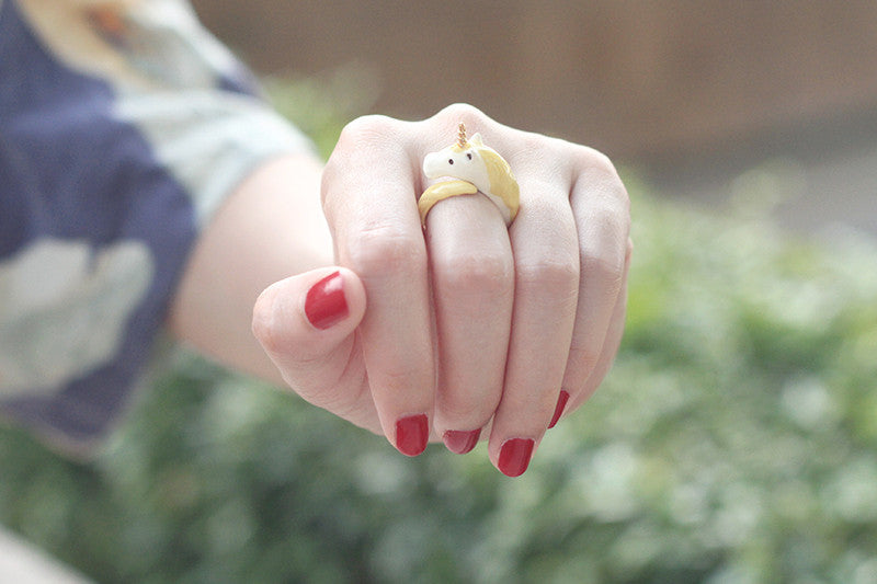 A close-up of a hand wearing a unicorn ring with red nails.