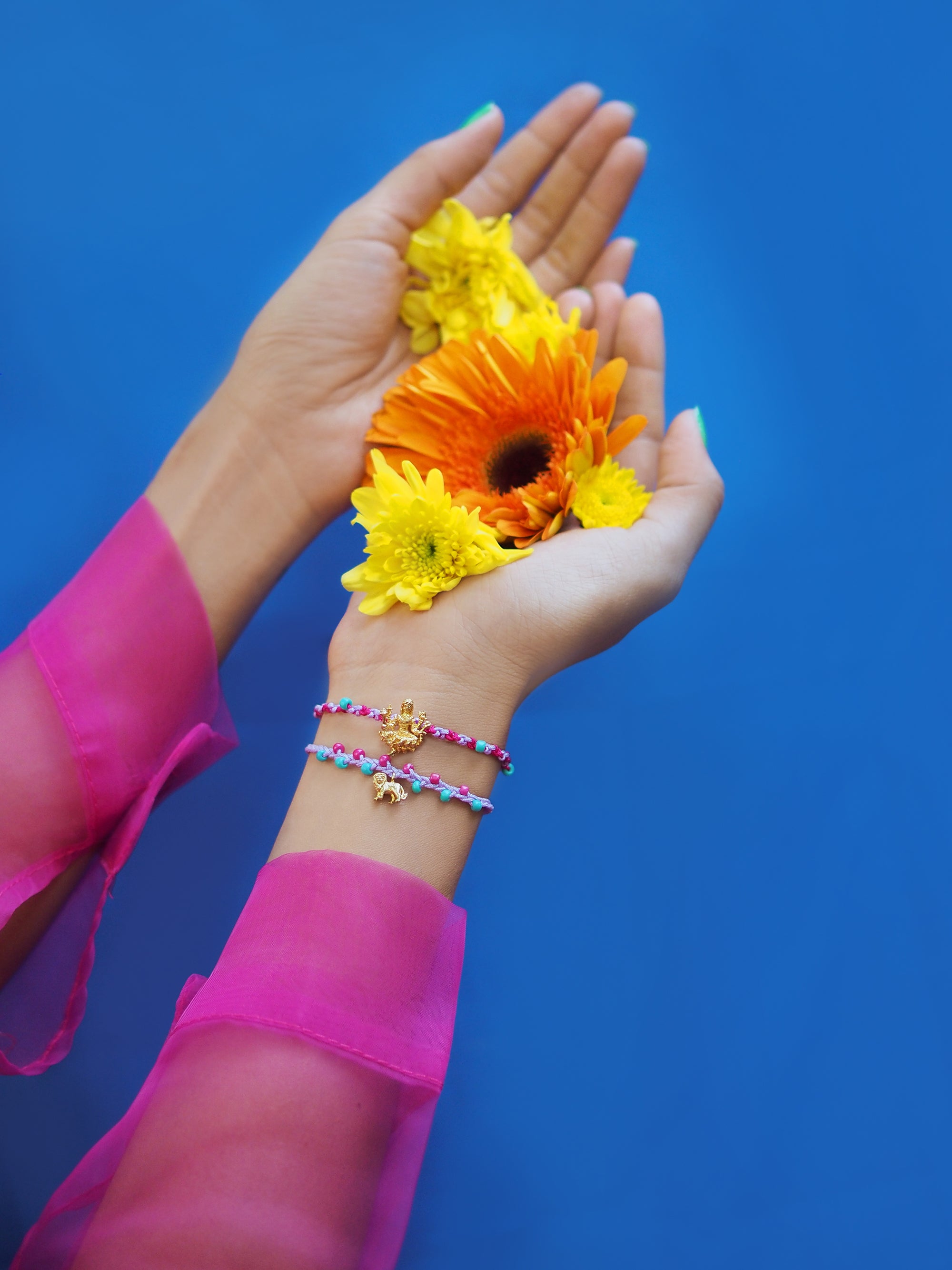 Close-up of a hand with a colorful Tridevi Parvati bracelet set while holding vibrant flowers.