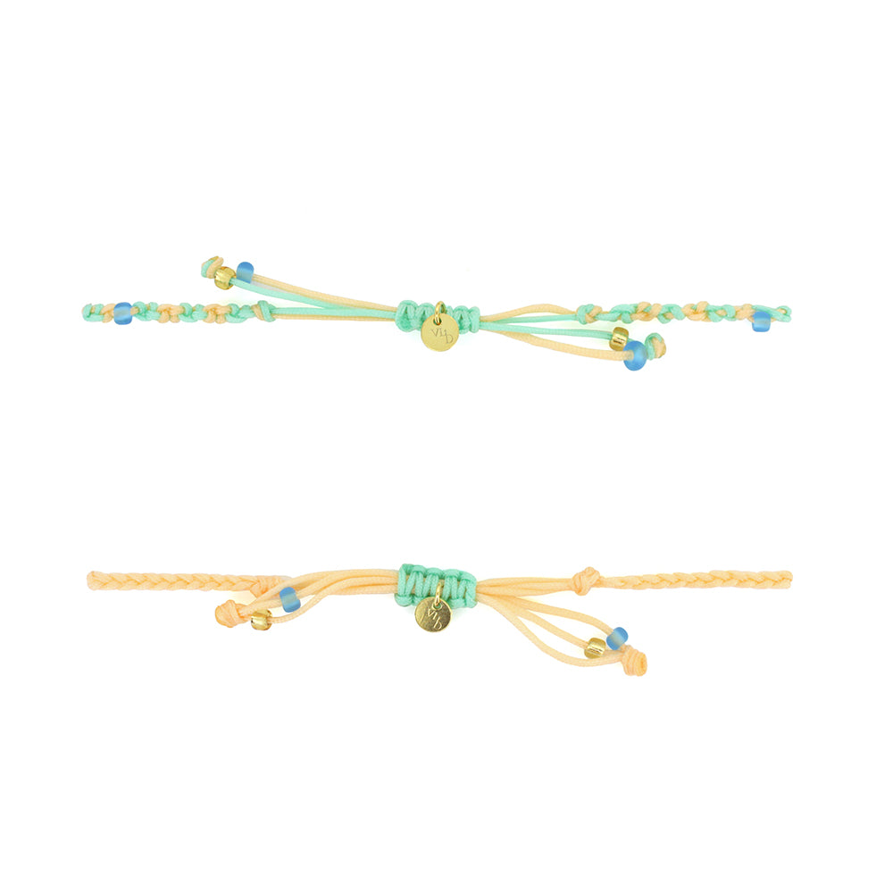 Two bracelets in pastel green and yellow threads with colorful beads, featuring a gold Tridevi Sarasvati charm and a gold peacock charm.