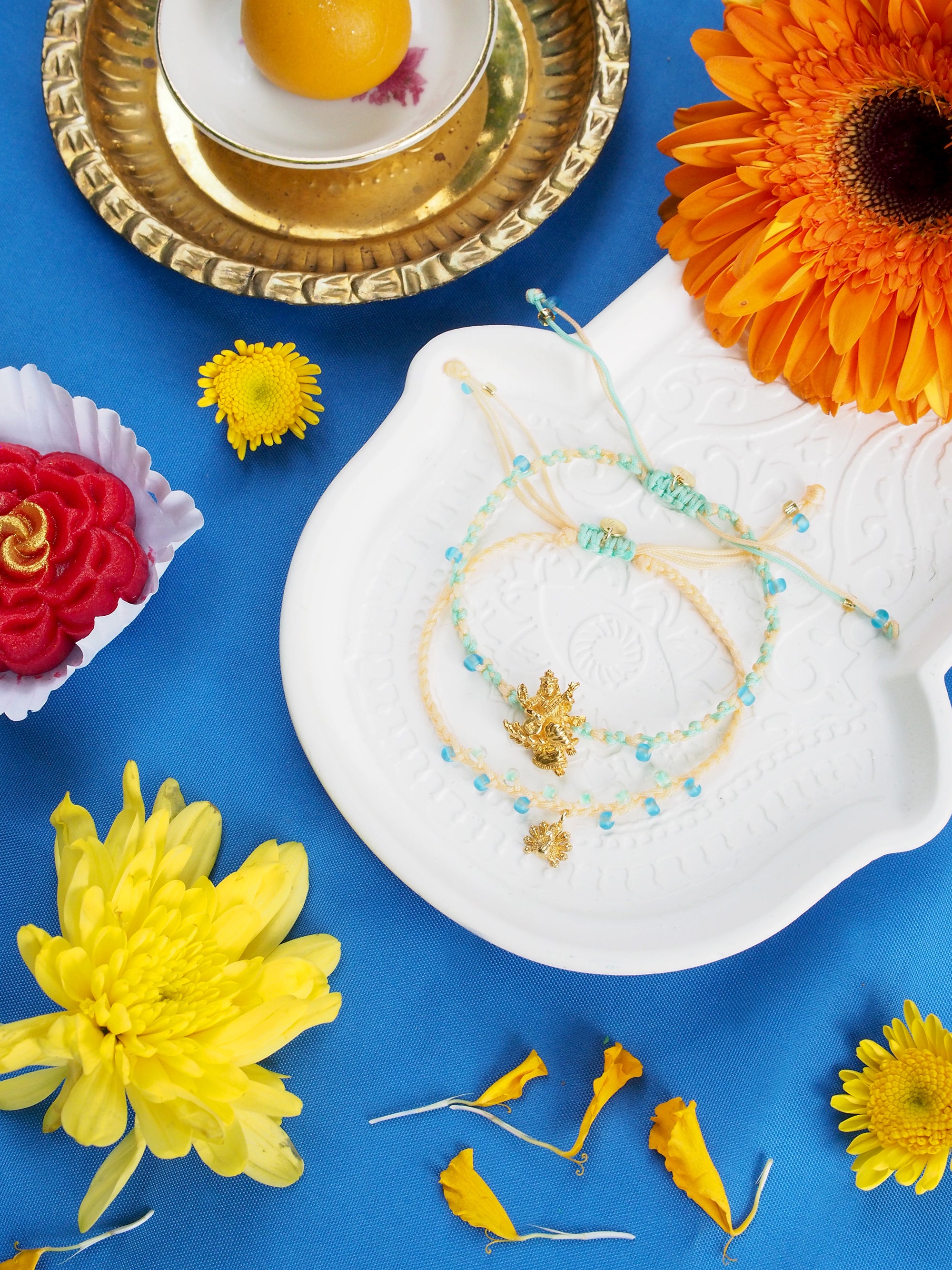 Two bracelets featuring a Tridevi Sarasvati charm and an peacock charm, surrounded by vibrant flowers.