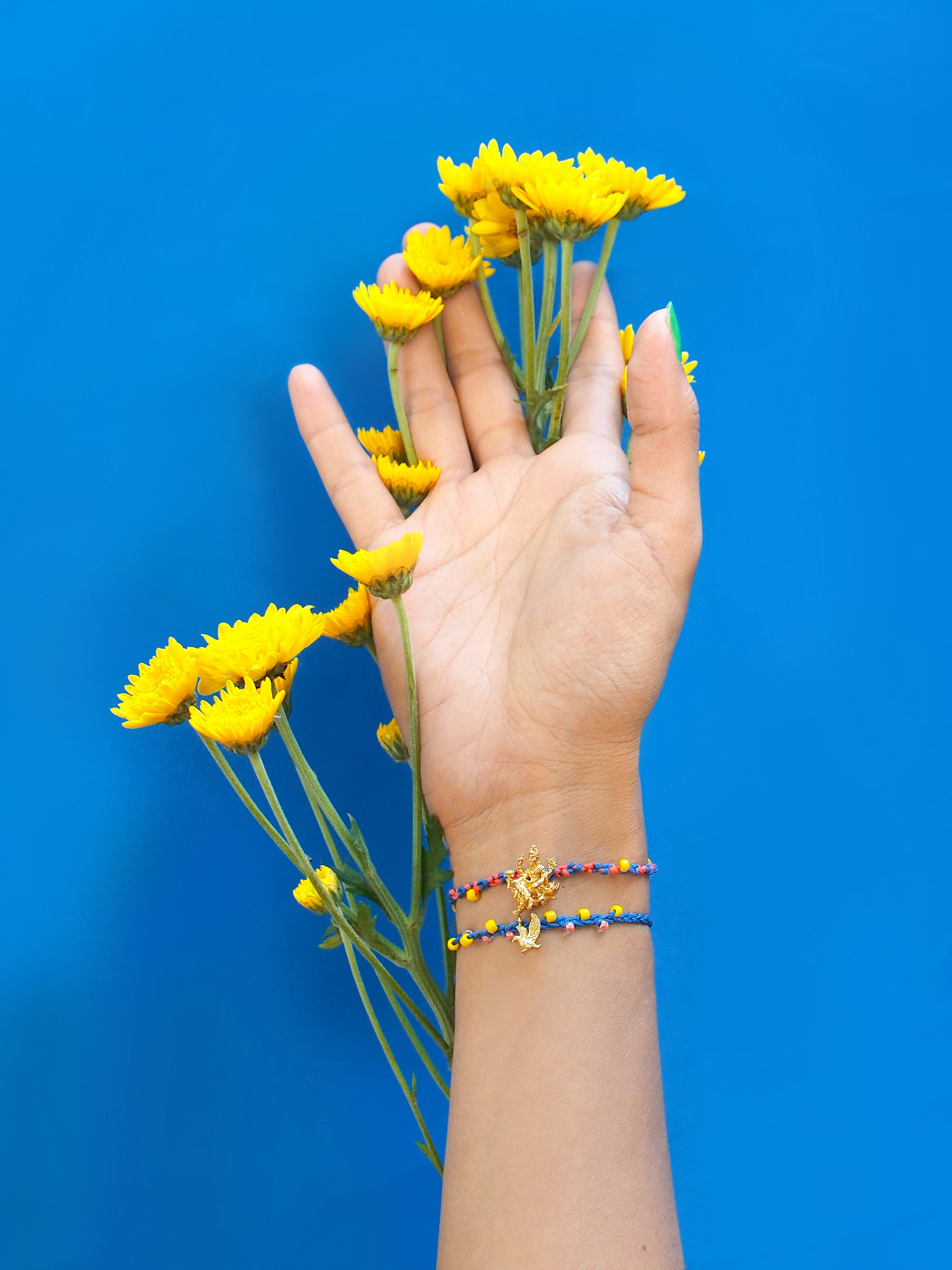 A hand adorned with a colorful Vishnu bracelet set among yellow flowers.