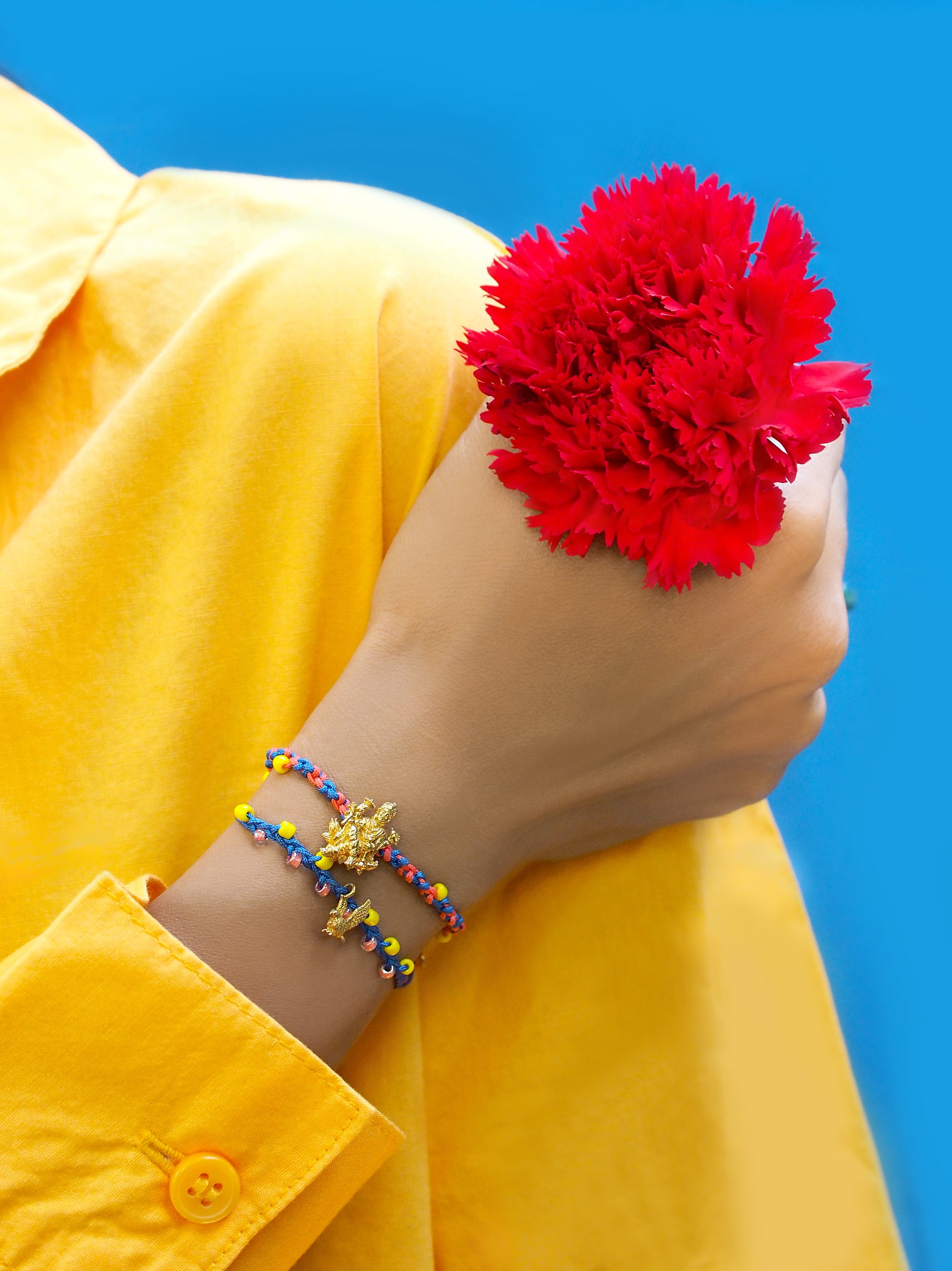 A person wearing a yellow shirt and a colorful Trimurti Vishnu bracelet set while holding a red flower.