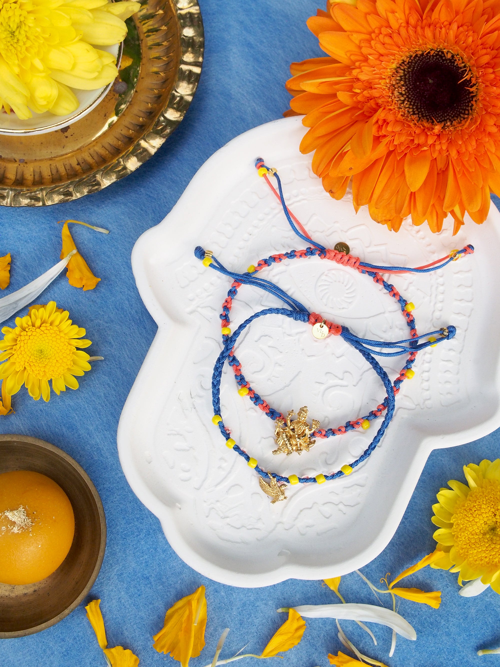 Two colorful bracelets featuring a gold Trimurti Vishnu charm and a gold garuda charm surrounded by vibrant flowers.