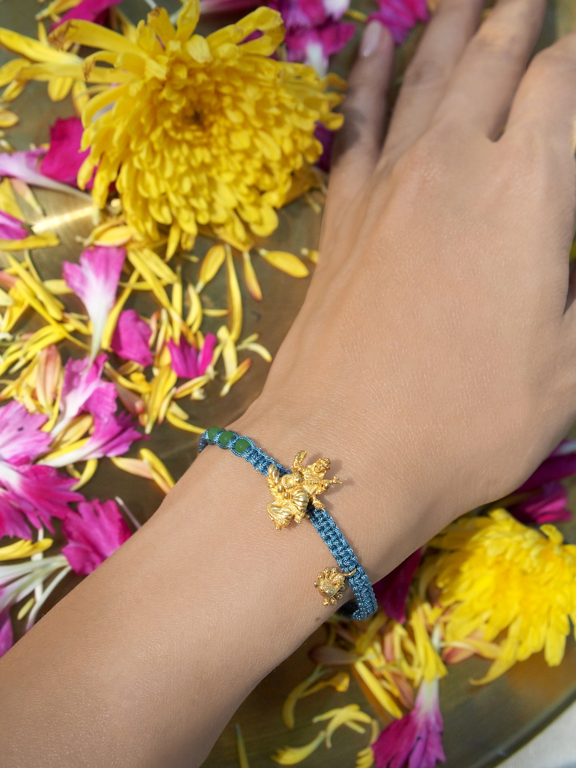 Close-up of a hand wearing a elegant Tridevi Sarasvati charm bracelet surrounded by vibrant flowers.