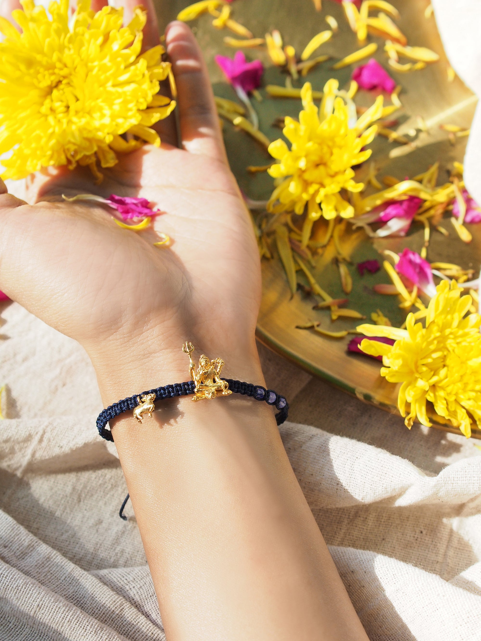 Close-up of an elegant bracelet featuring a gold Trimurti Shiva charm with amethyst-faced beads surrounded by vibrant flowers.