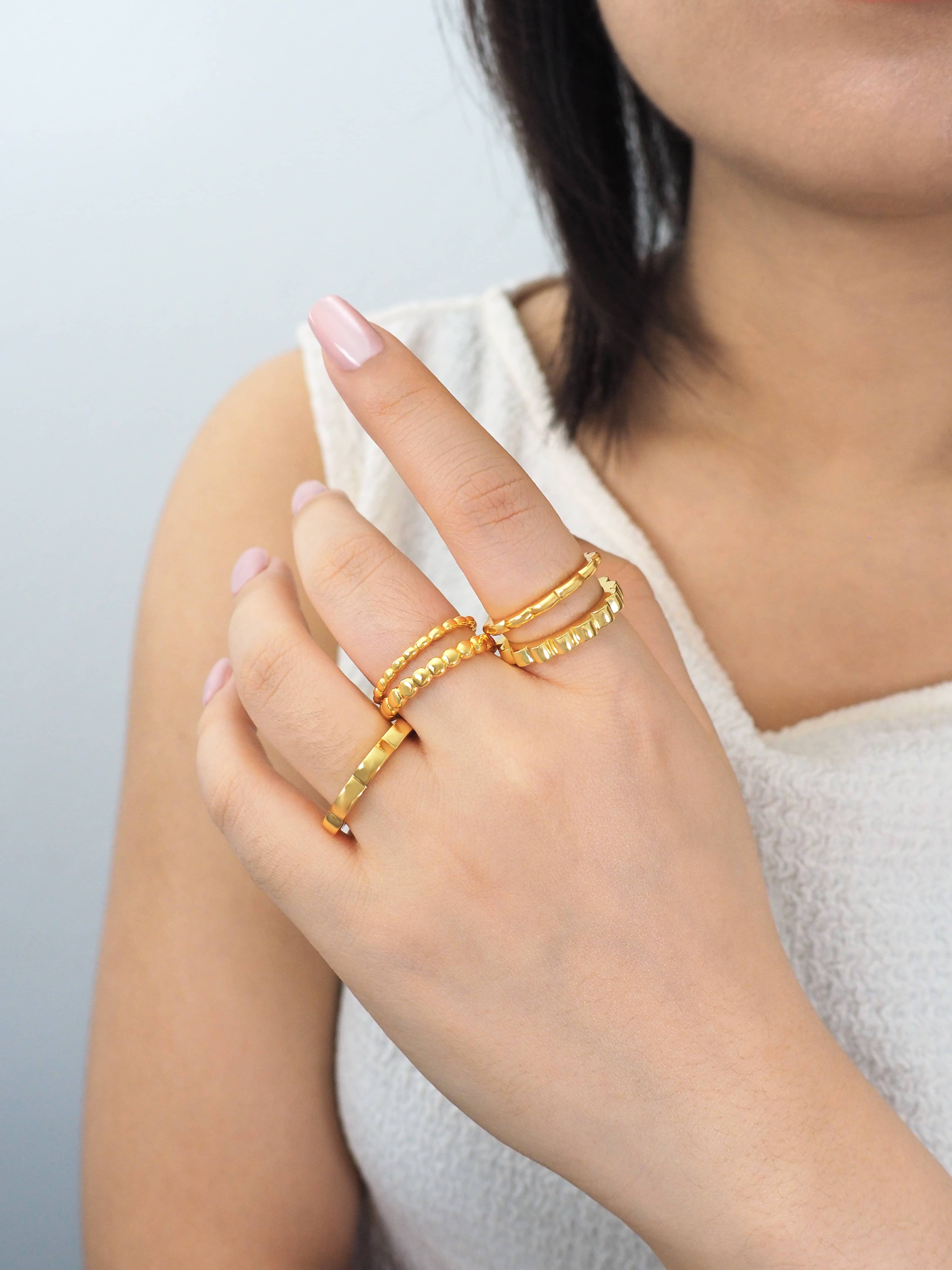 Model wearing modern design of gold-plated stacking rings on fingers in casual outfit.