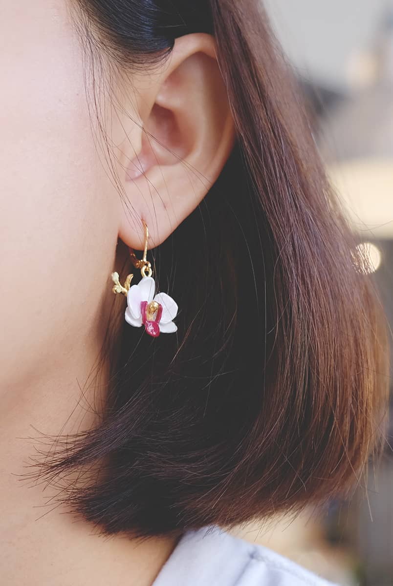 A close-up of a woman wearing floral earrings with a white phalaen design