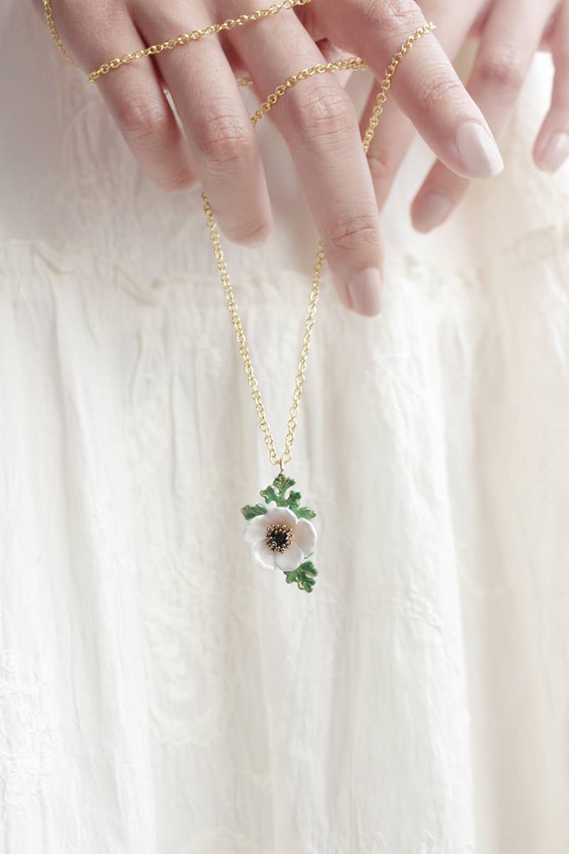 A model holding stunning flower pendant necklace featuring a light pink, white flower and green leaves.