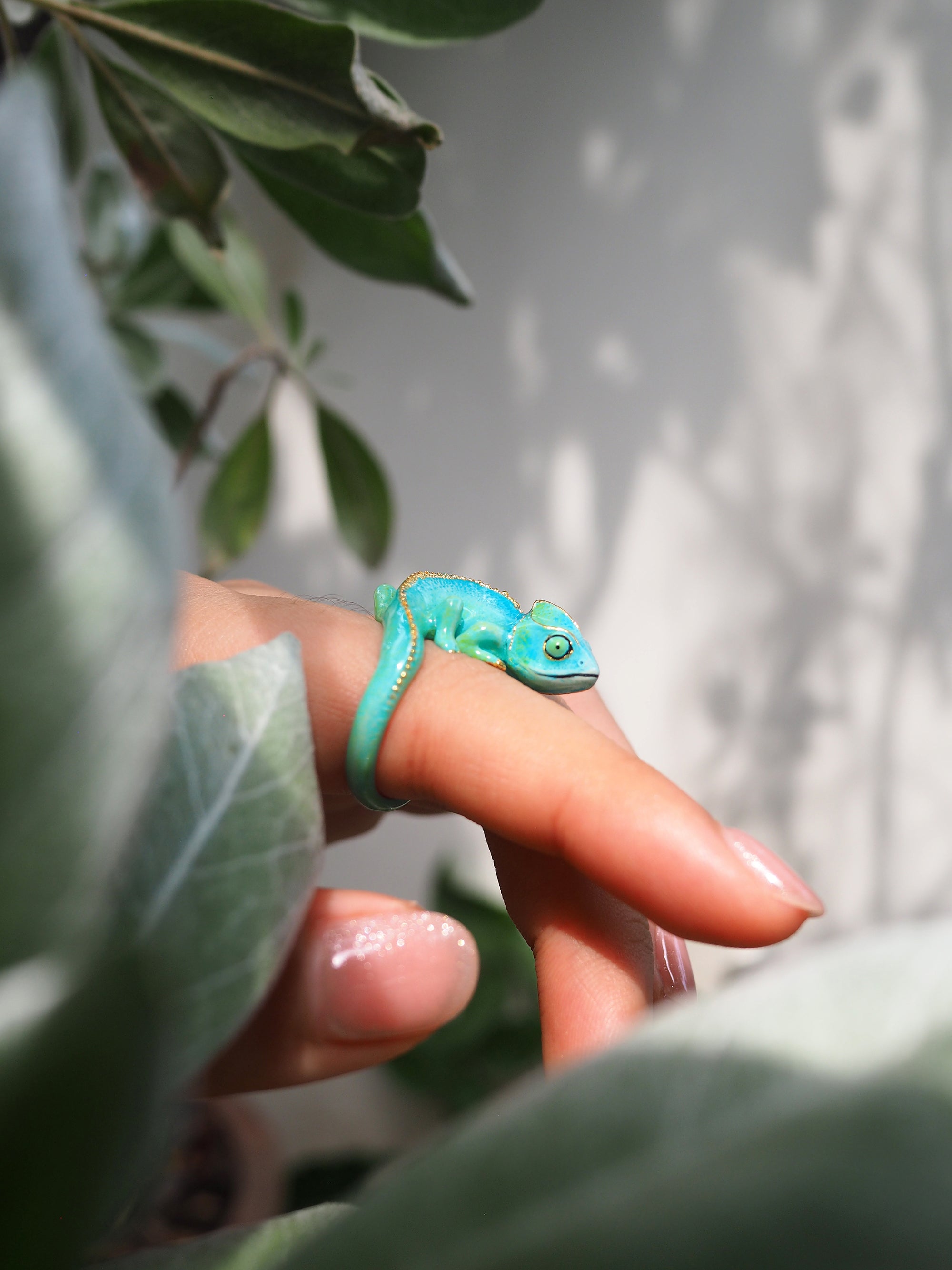 Nature-inspired chameleon ring displayed on a hand among green leaves.