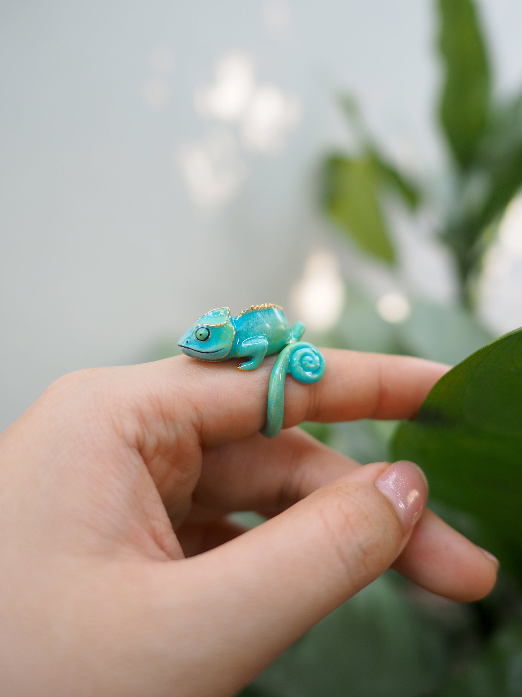 Close-up of a vibrant chameleon ring displayed on a finger surrounded by greenery.