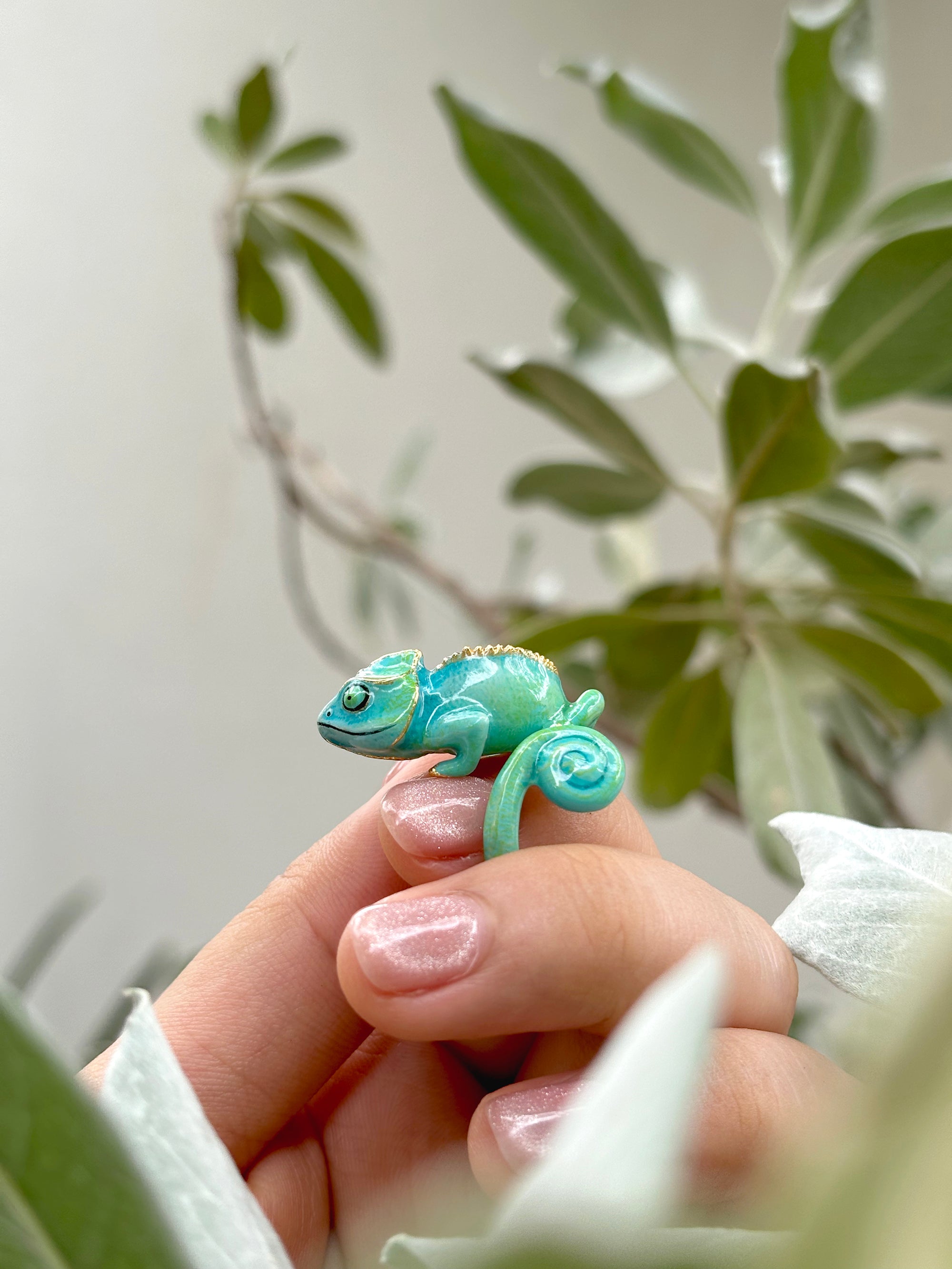 Close-up of a vibrant chameleon ring rested on a finger surrounded by greenery.