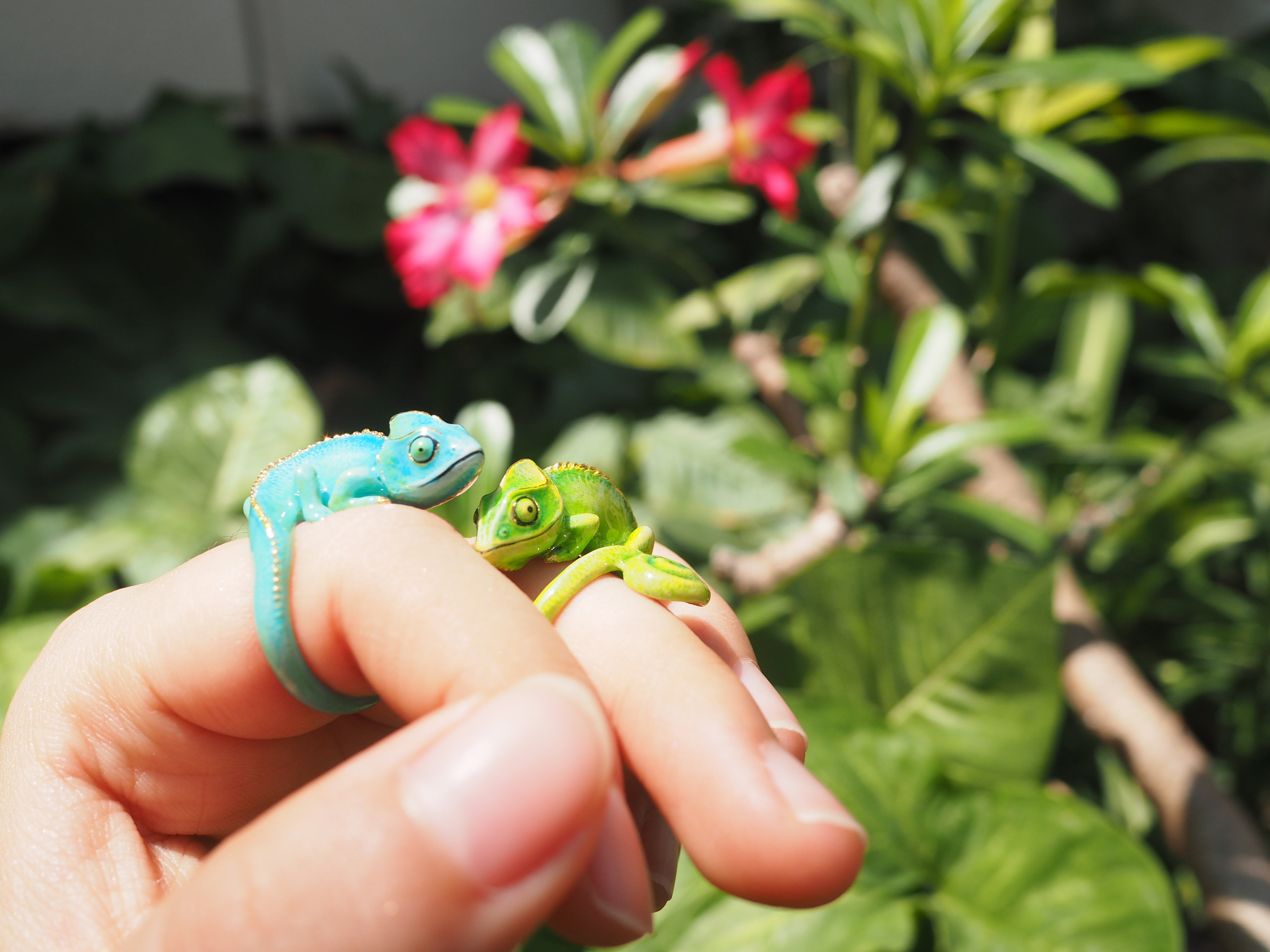 Playful design of chameleon rings on a hand in a garden setting.