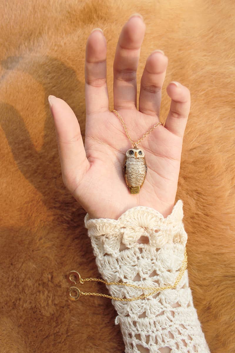 Hand holding a whimsical owl whistle necklace with a gold chain.