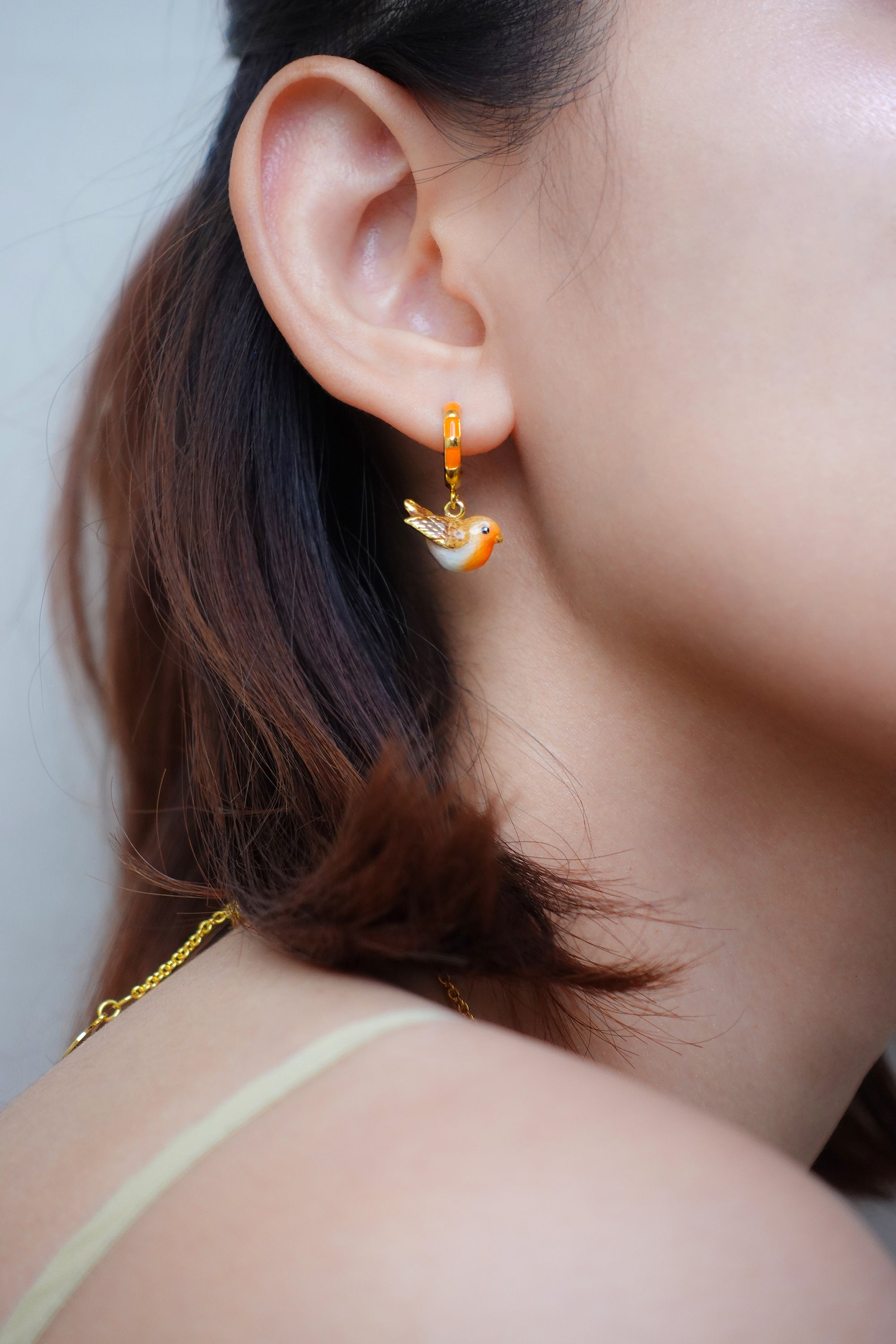 Close-up of a model wearing an orange bird-shaped earring.
