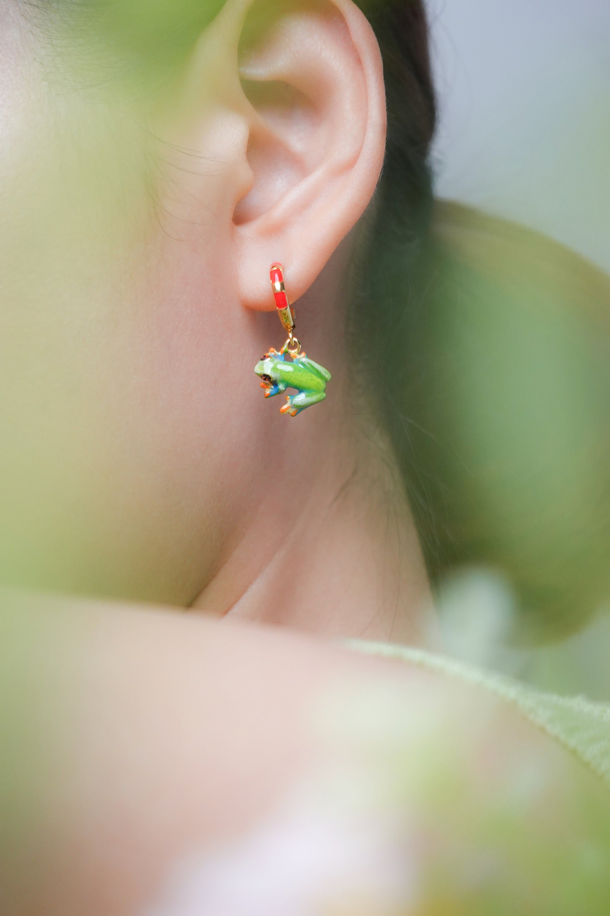 Unique green frog earrings worn by a model, showcasing a playful design.
