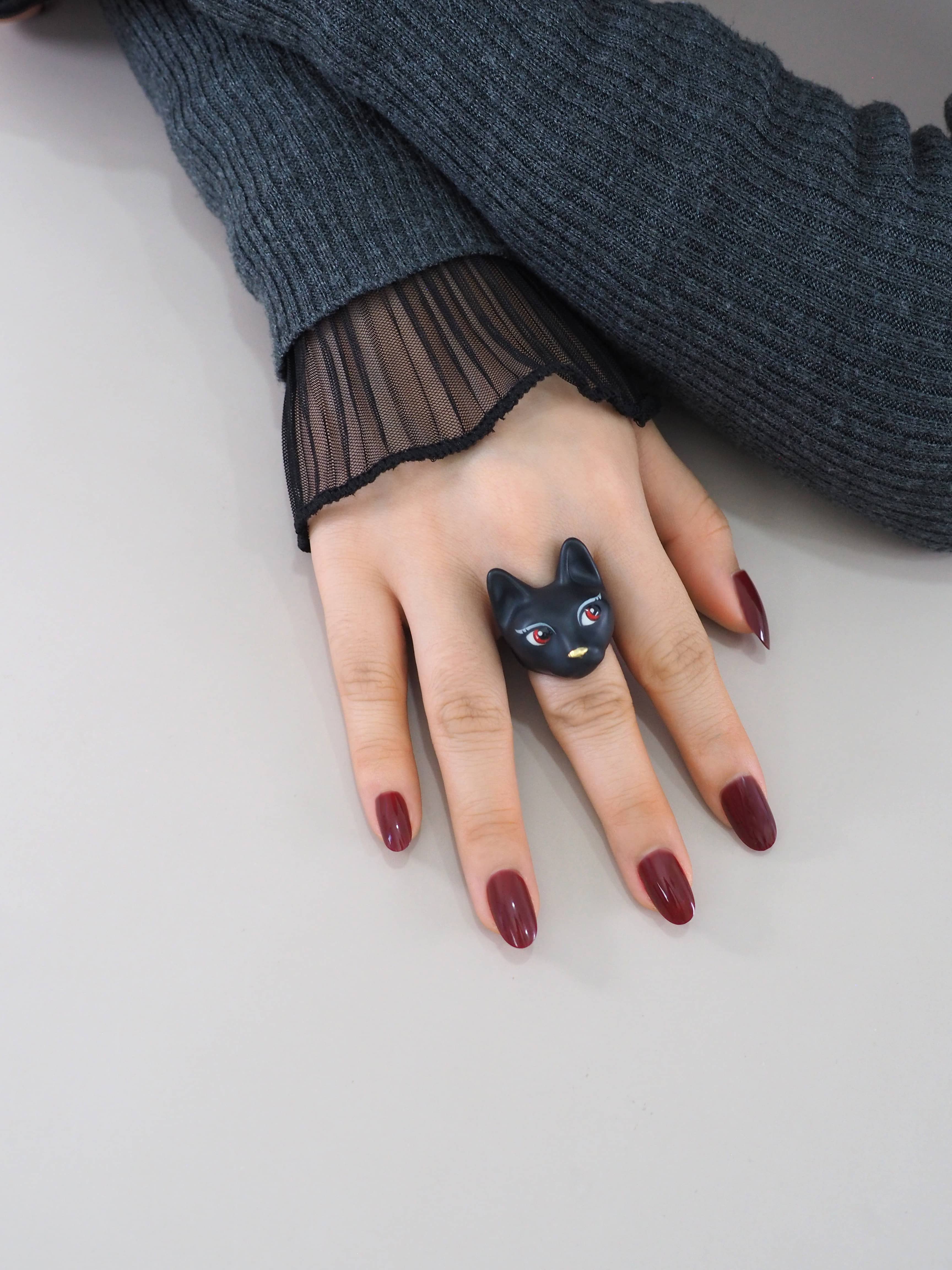 A model wearing a hand-painted ring featuring a black cat with red eyes.