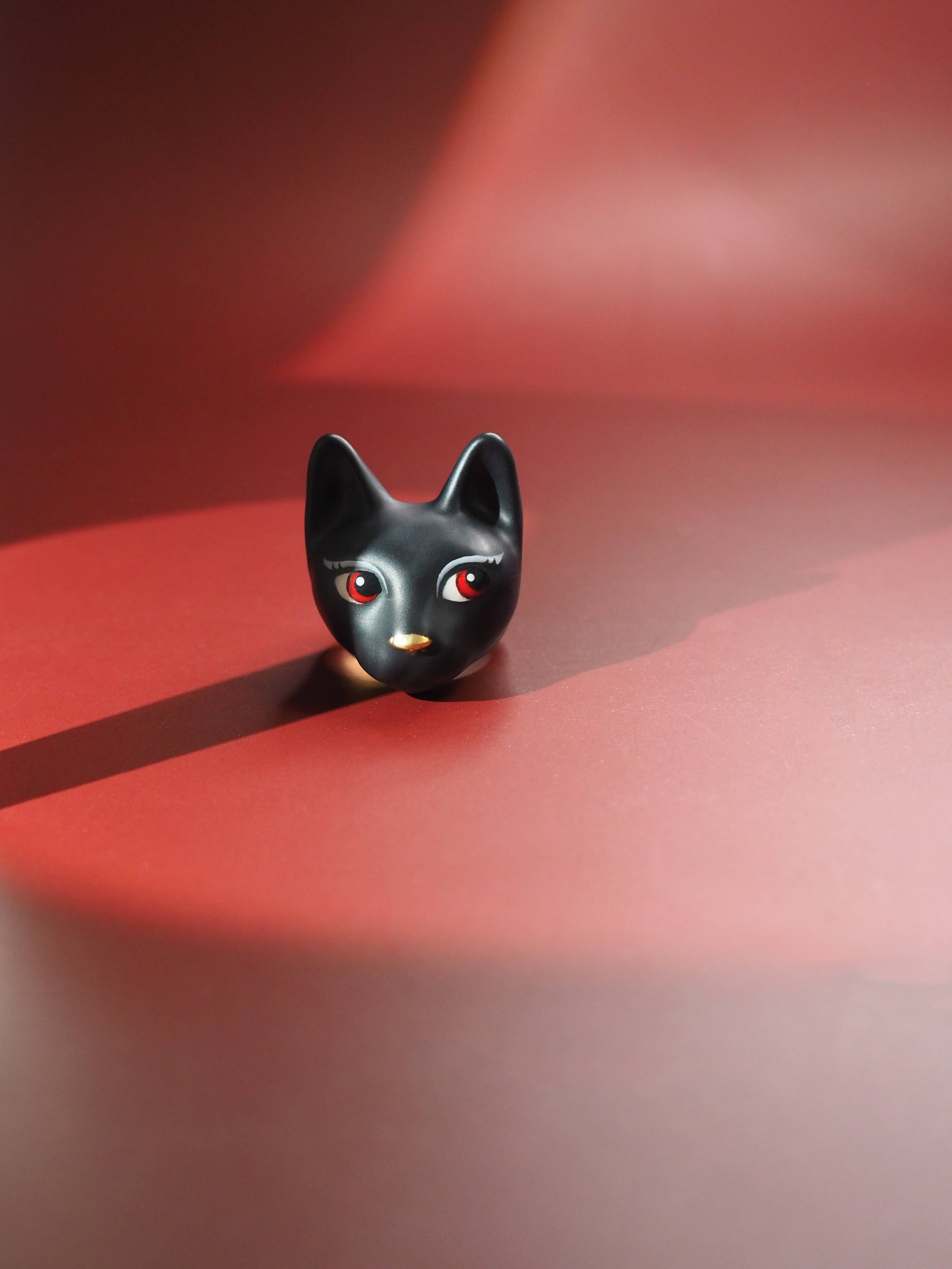 A hand-painted ring showcasing a black cat with fierce red eyes placed on red background.