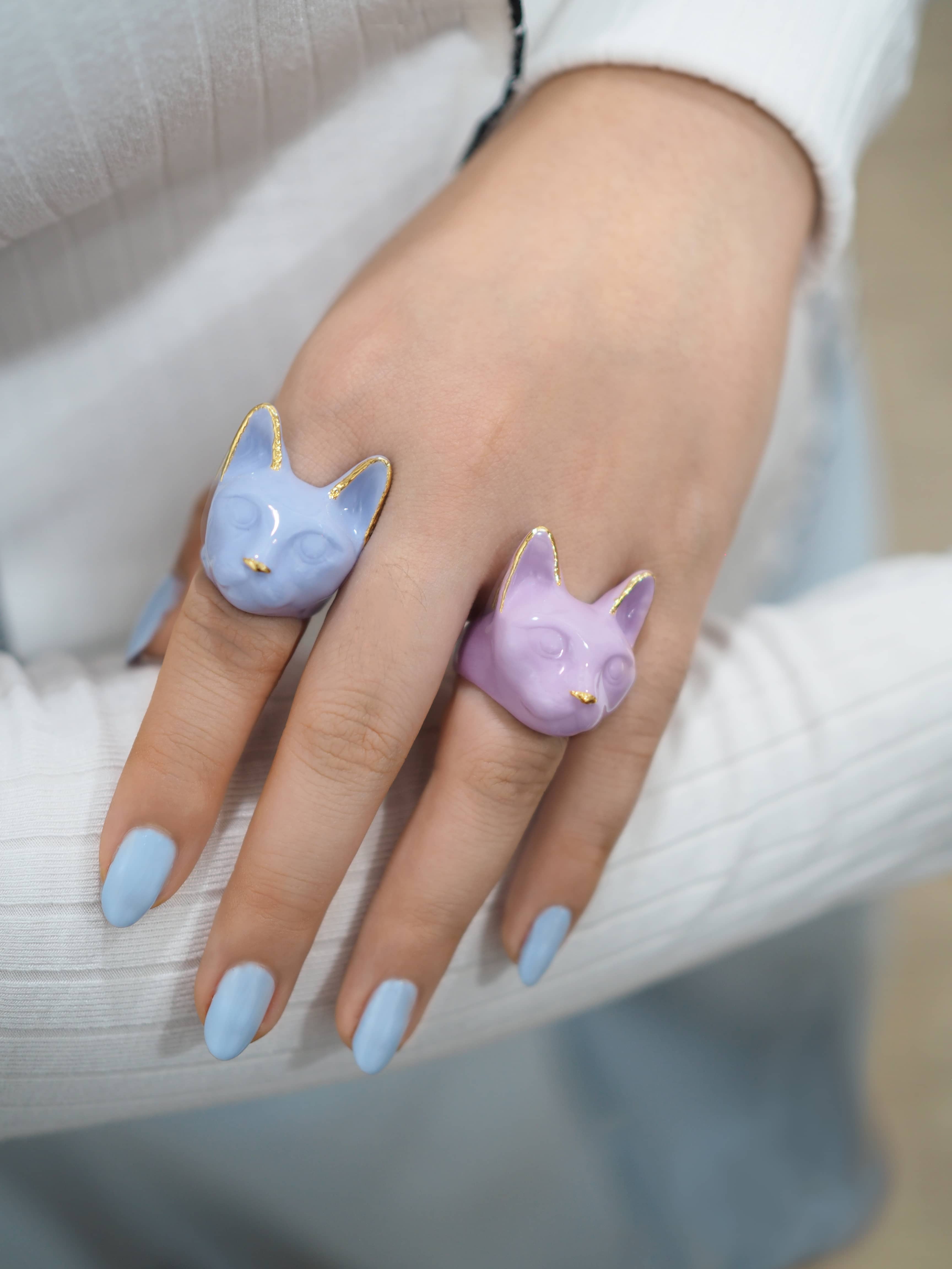 Close up of two cat rings featuring pastel colors worn on a person's hand.