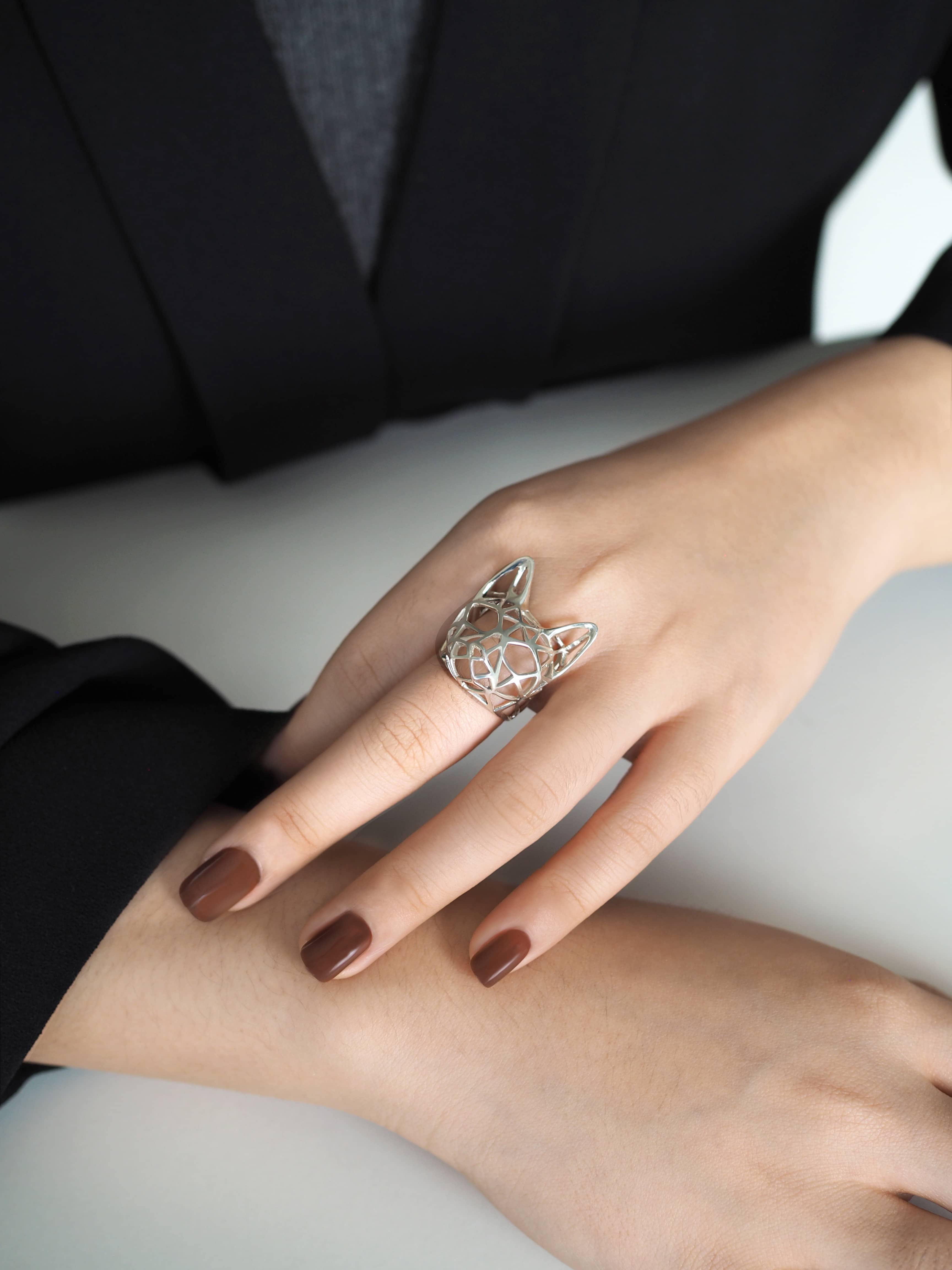 Modern jewelry design featuring a cat-shaped ring in silver on a woman's hand.
