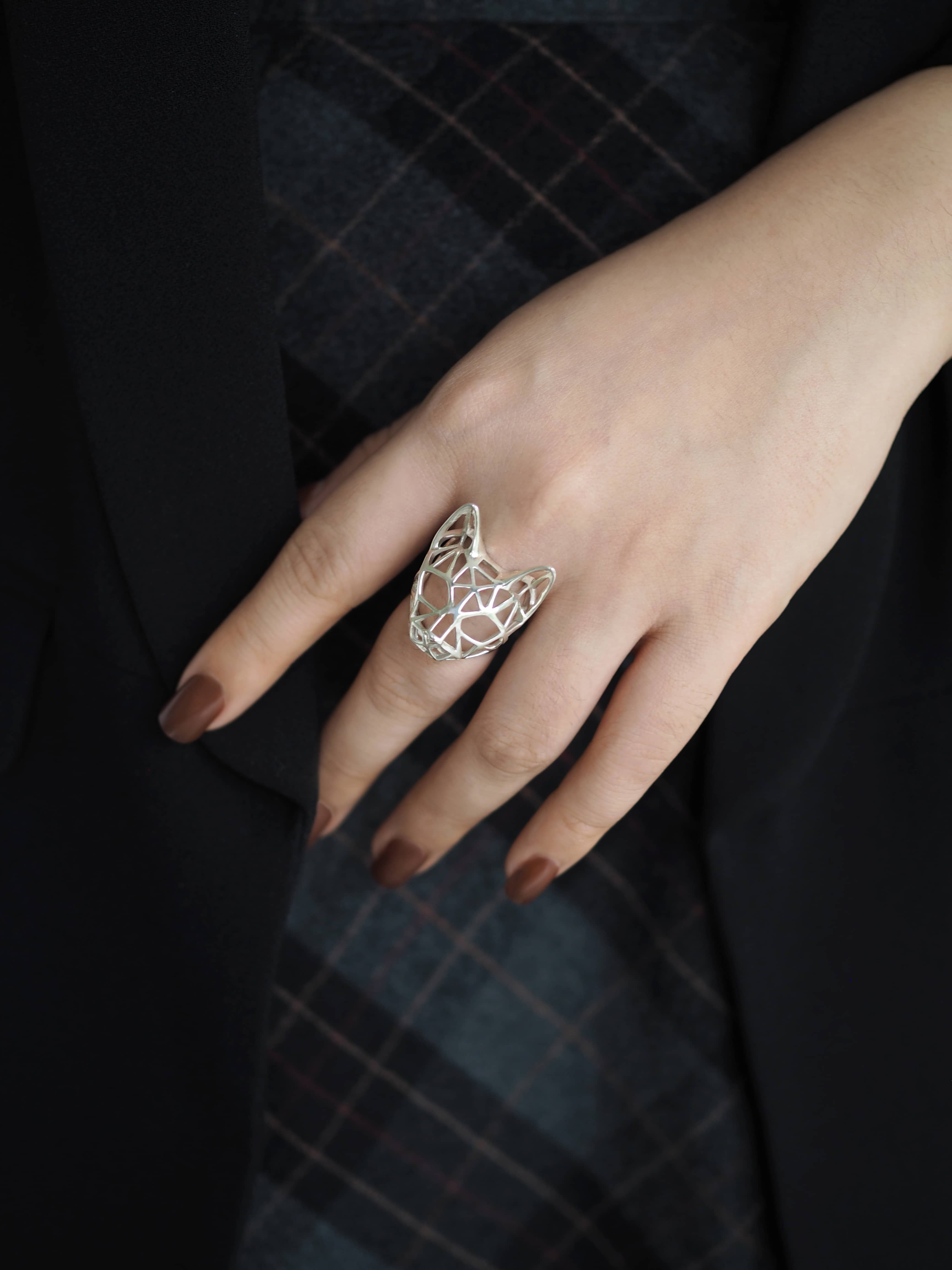 Fashion accessory ring with a cat motif, displayed on a hand with brown nails.