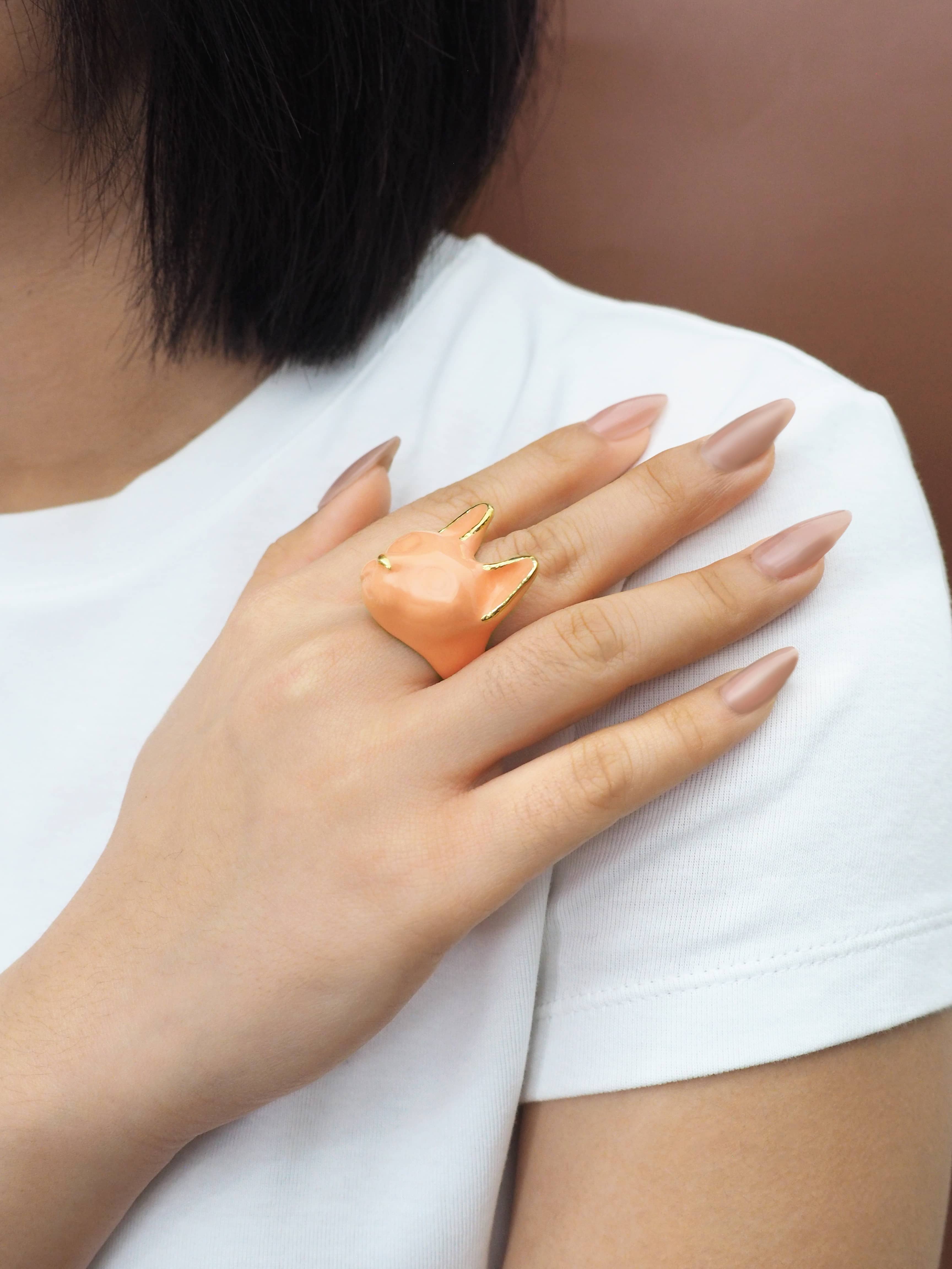 A hand wearing orange cat ring with white tee