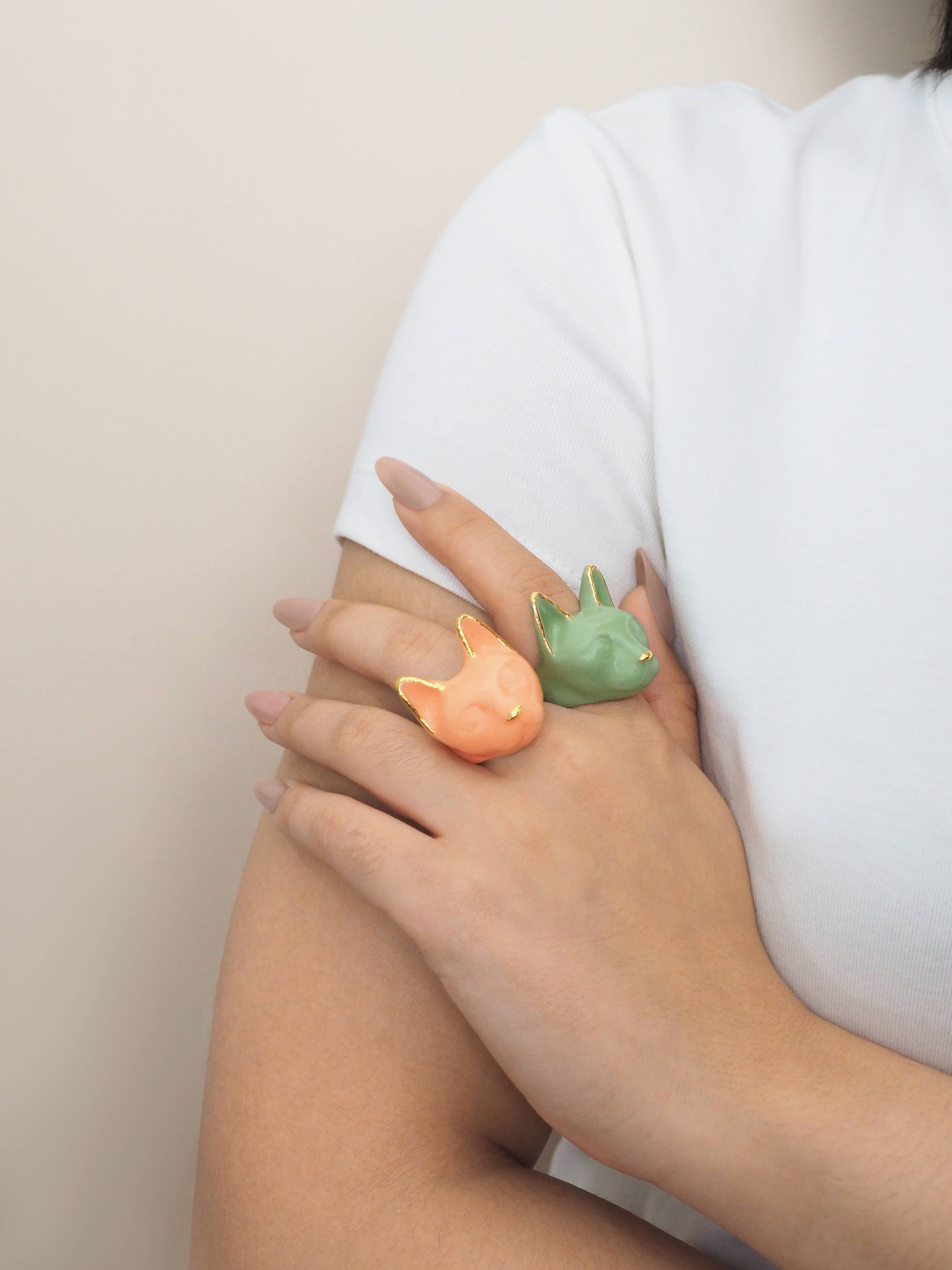 A hand wearing two cat rings: orange and green, perfect for fall vibes.
