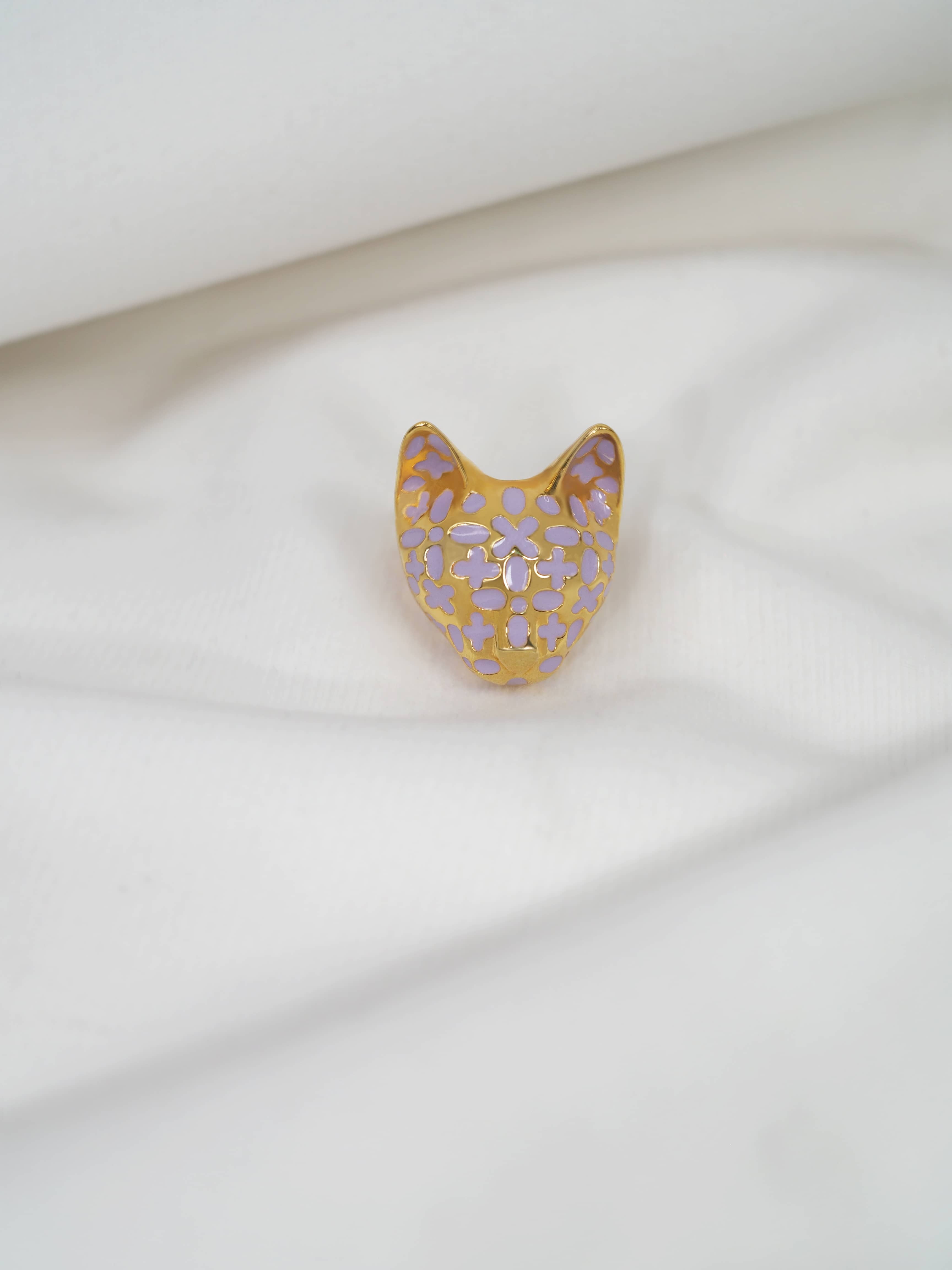 Elegant gold cat ring with lilac-inspired design placed on white fabric.