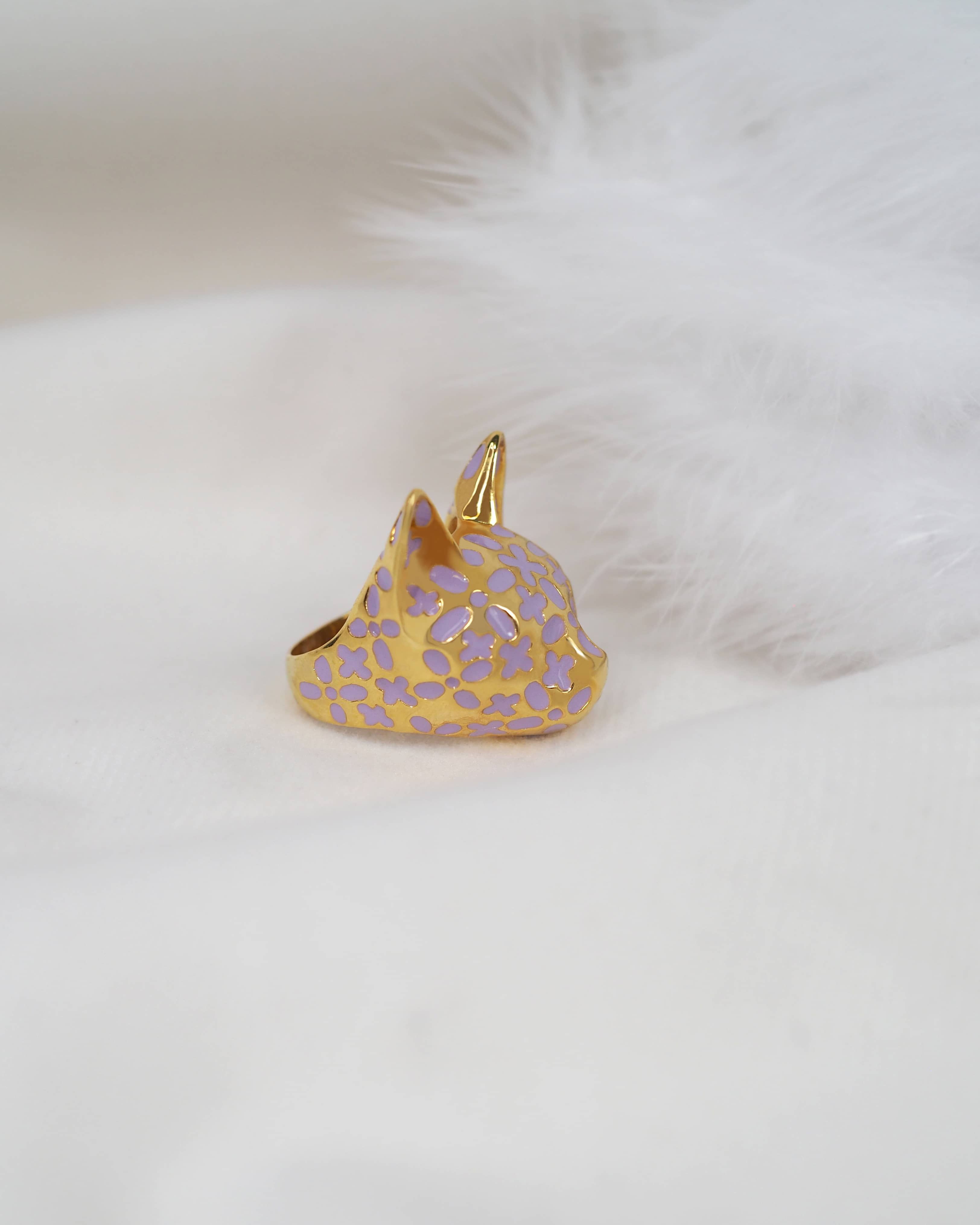 Stunning gold cat ring with purple flower patterns placed on white fabric.