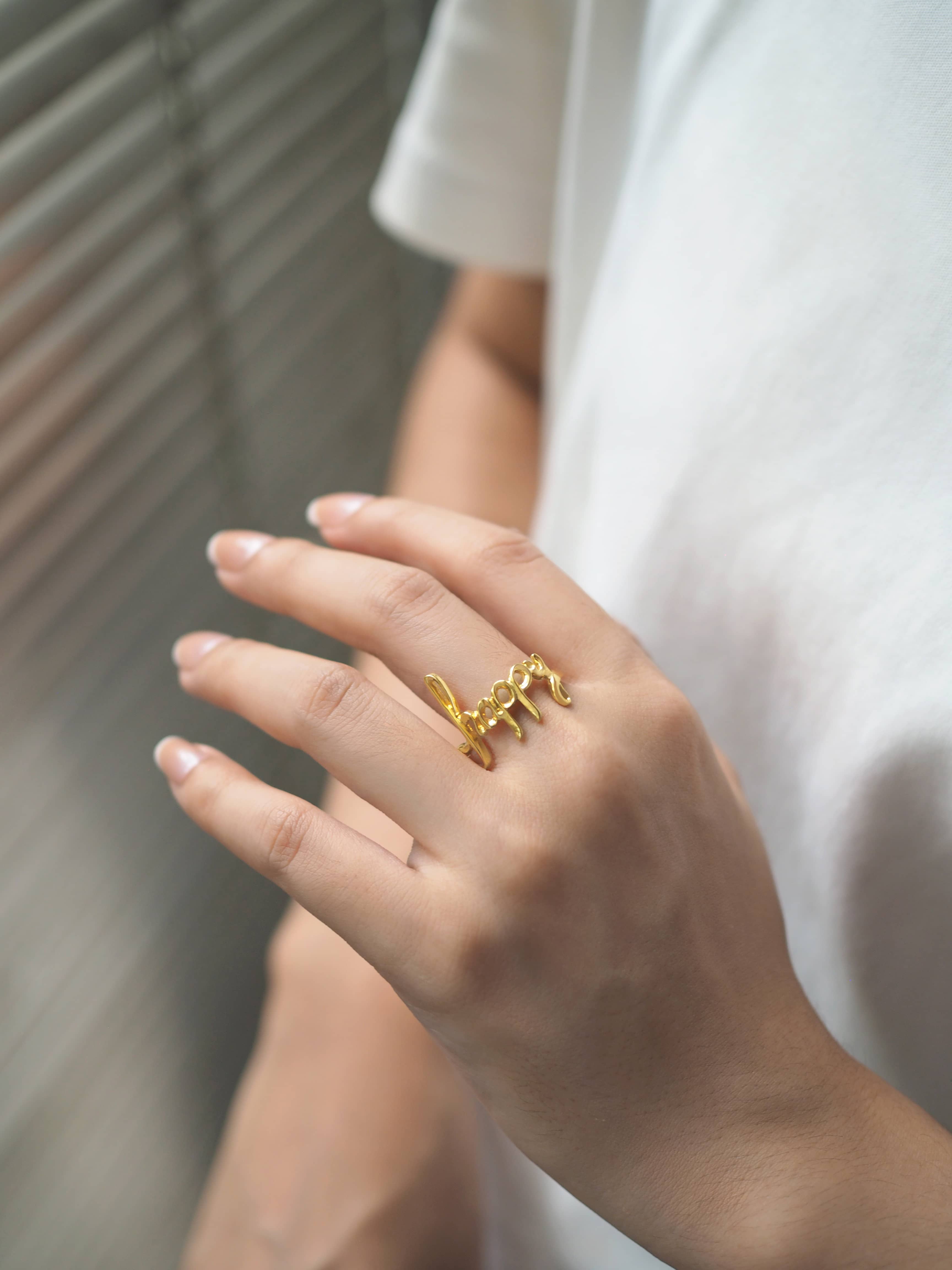 Close-up of a hand wearing a gold ring with the word 'happy'