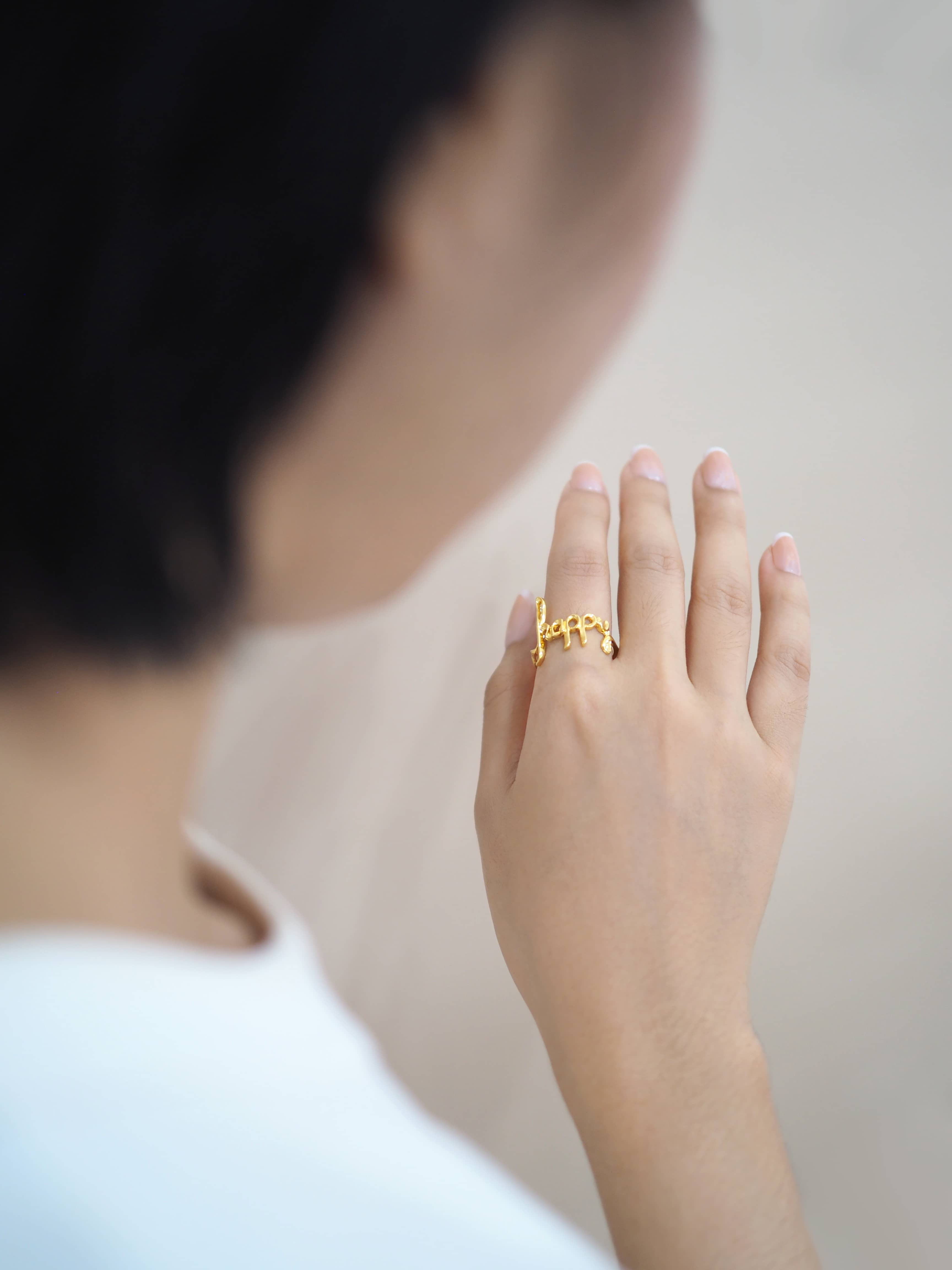 A hand wearing a gold ring with the word 'happy' with casual outfit.