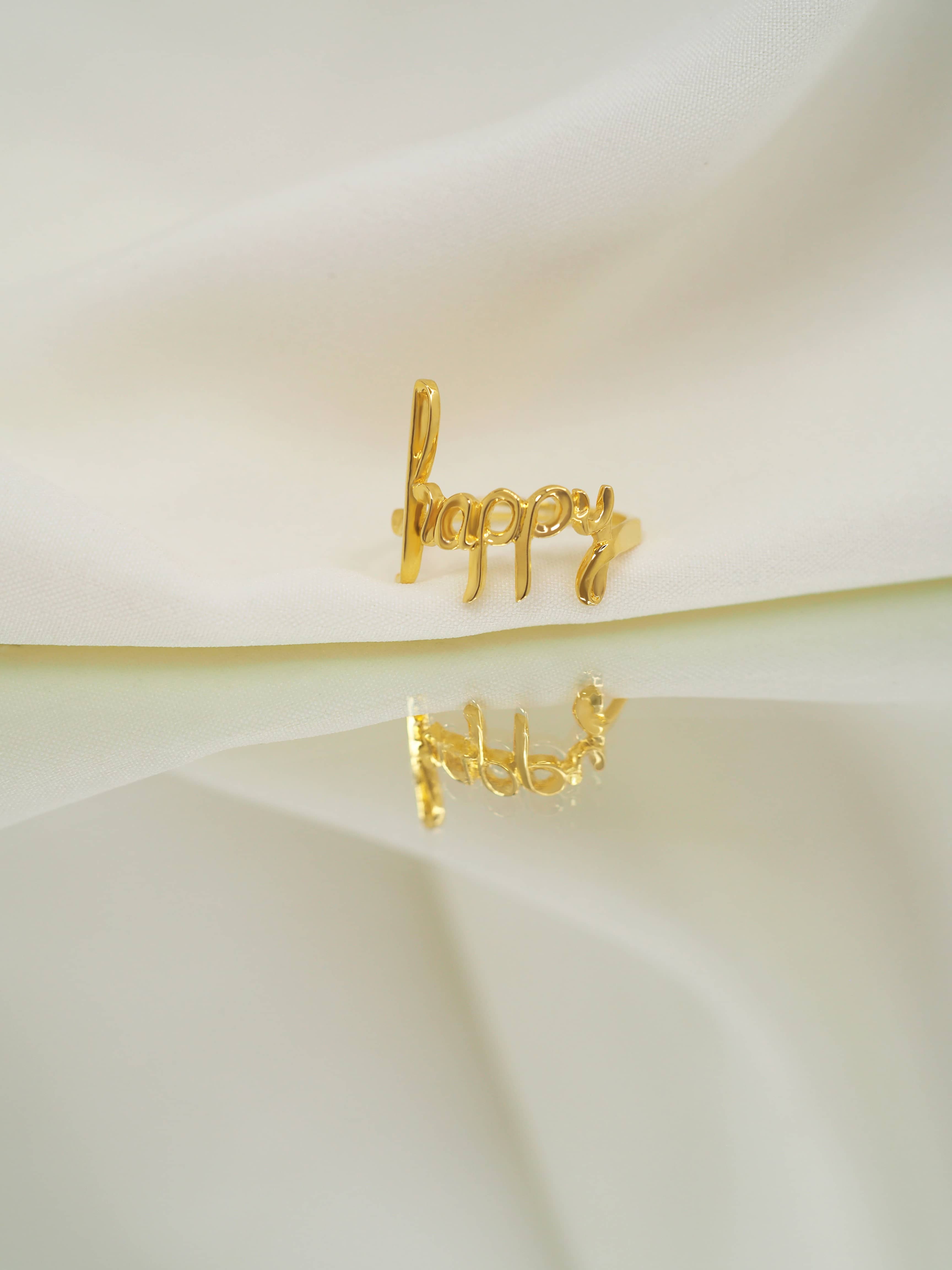 Beautiful designed gold ring featuring the word 'happy' in a handwritten style placed in soft color setting.