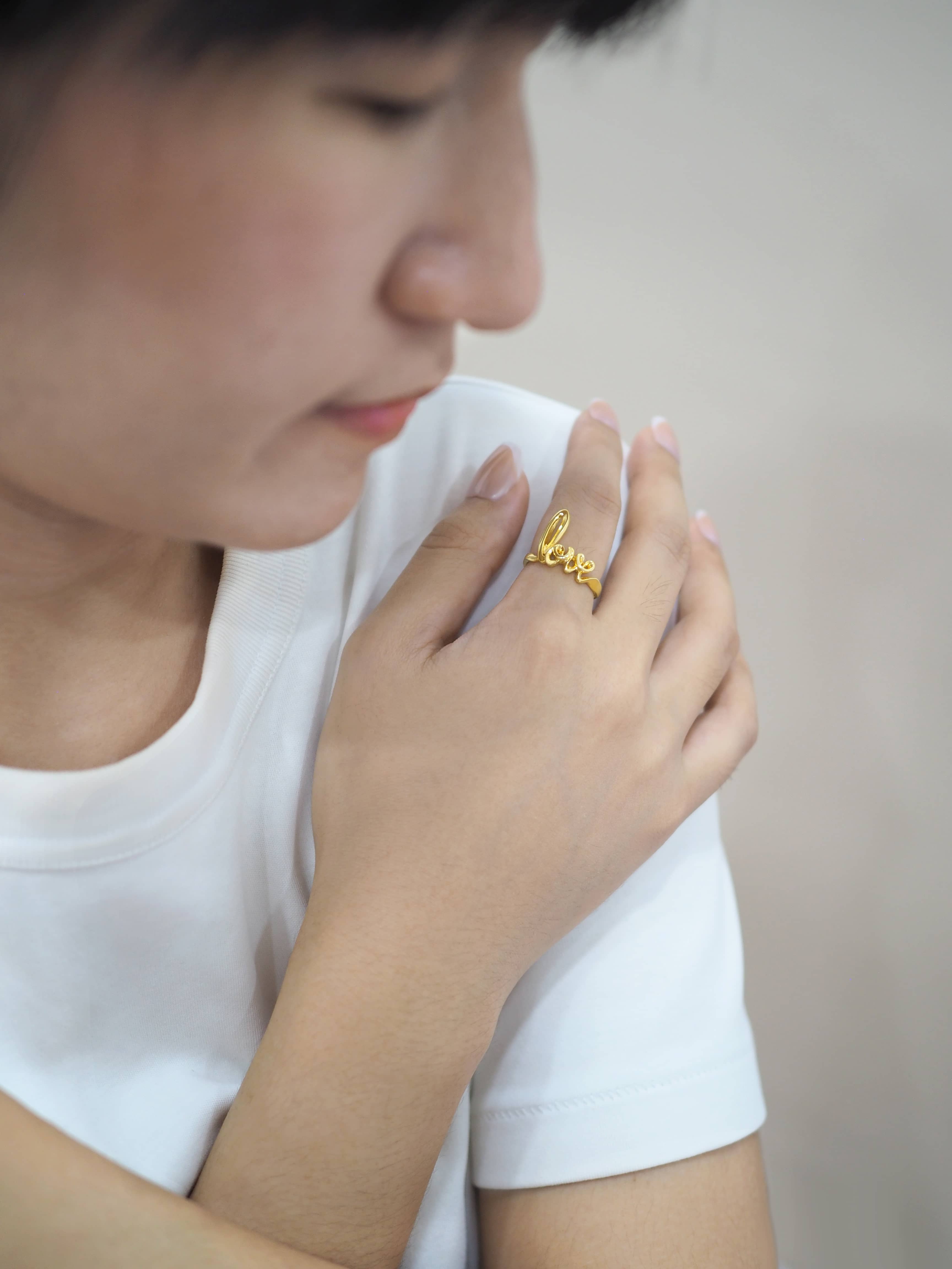 A hand wearing a gold ring with the word 'love' with white tee.